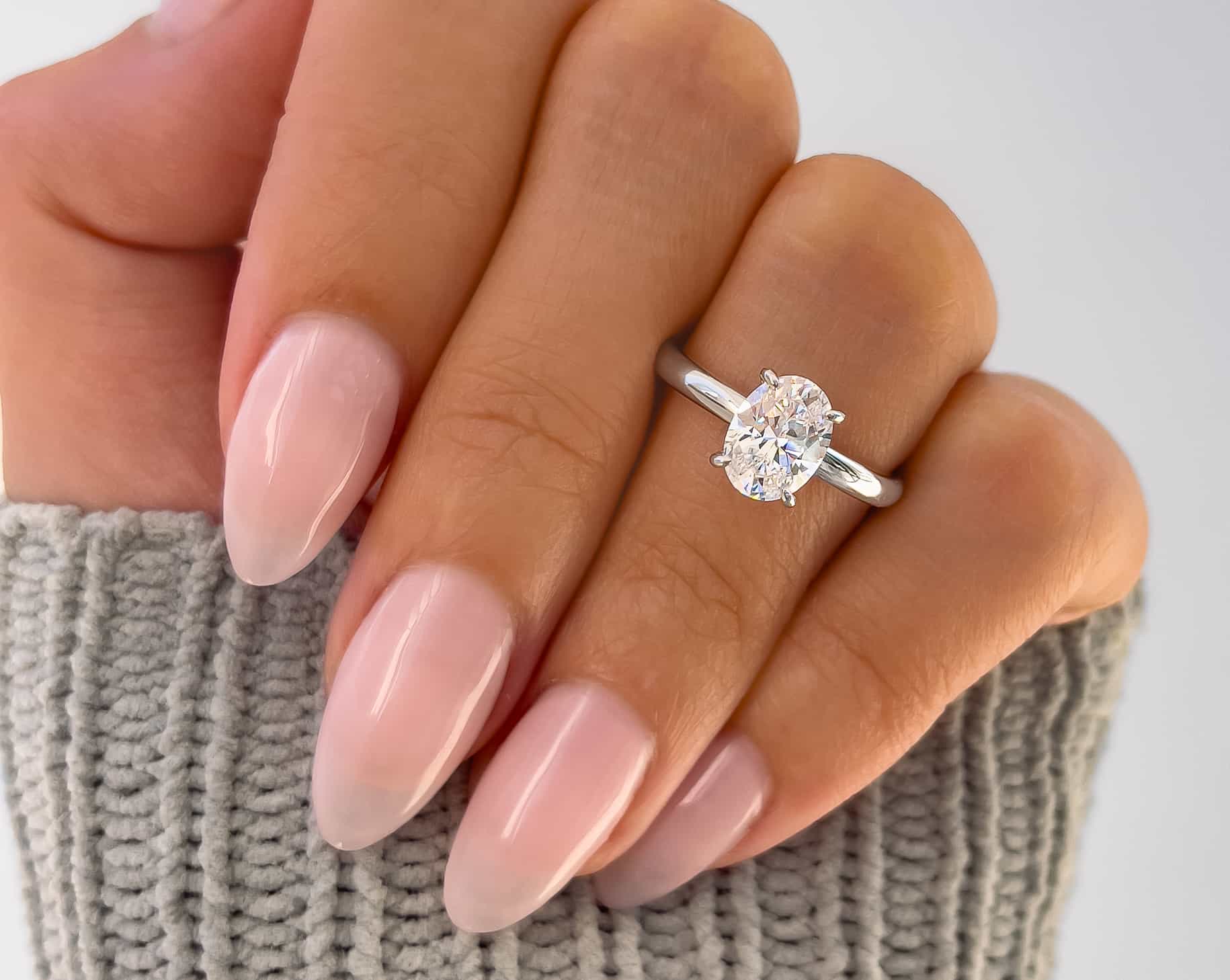 silver oval cut engagement ring on ladies hand with green sweater