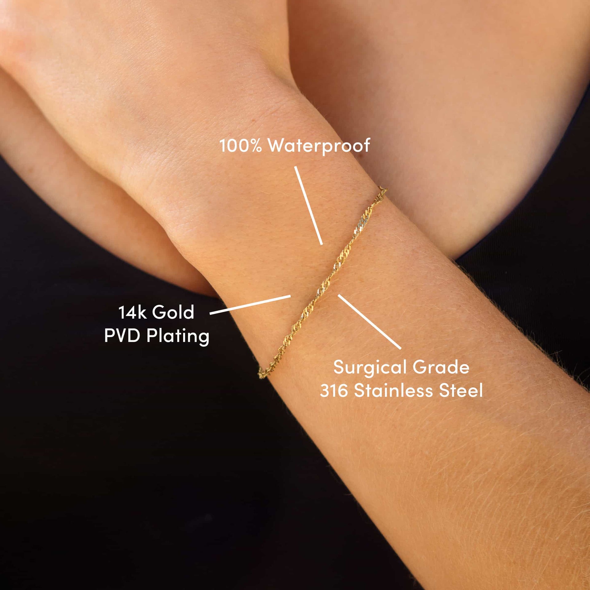 a close up of a dainty 14k gold PVD plated stainless steel singapore chain bracelet worn by a model with the text overlayed "tarnish resistant, 100% waterproof, & surgical grade 316 stainless steel" 