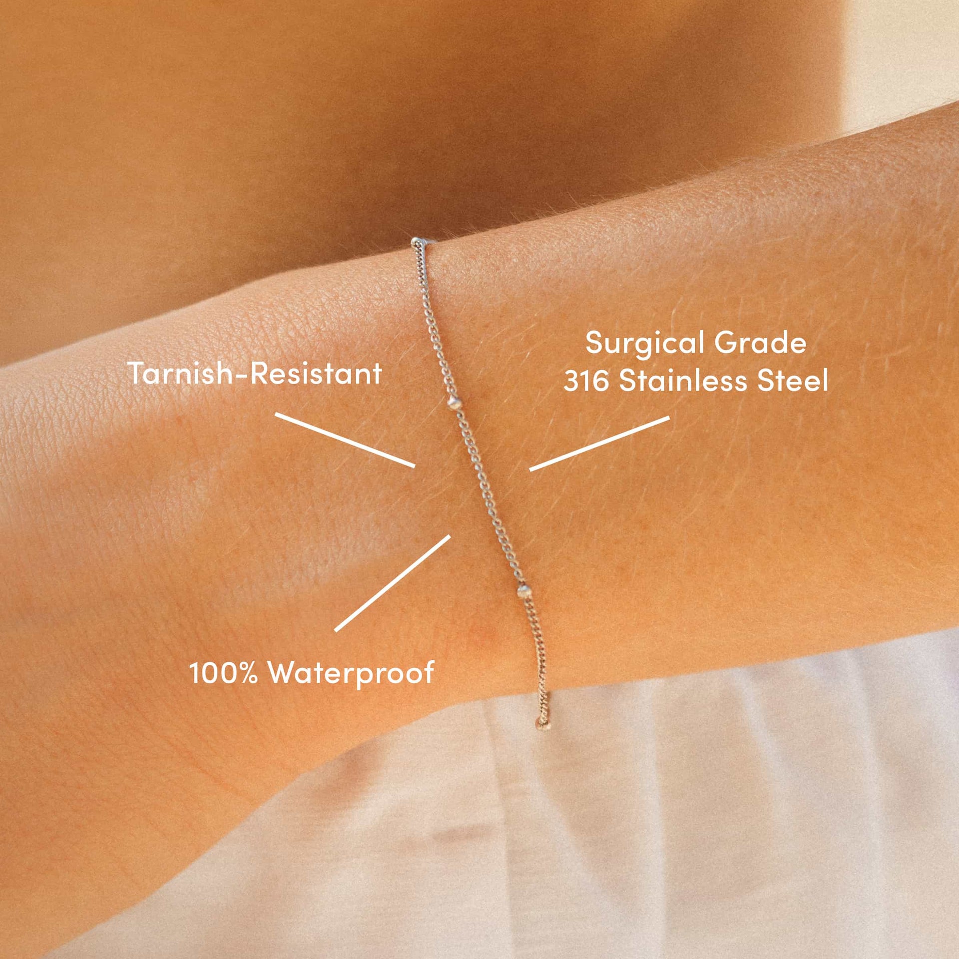 close up of dainty stainless steel satellite bracelet labeled with "100% Waterproof, Tarnish-Resistant, & Surgical Grade 316 Stainless Steel" on a model