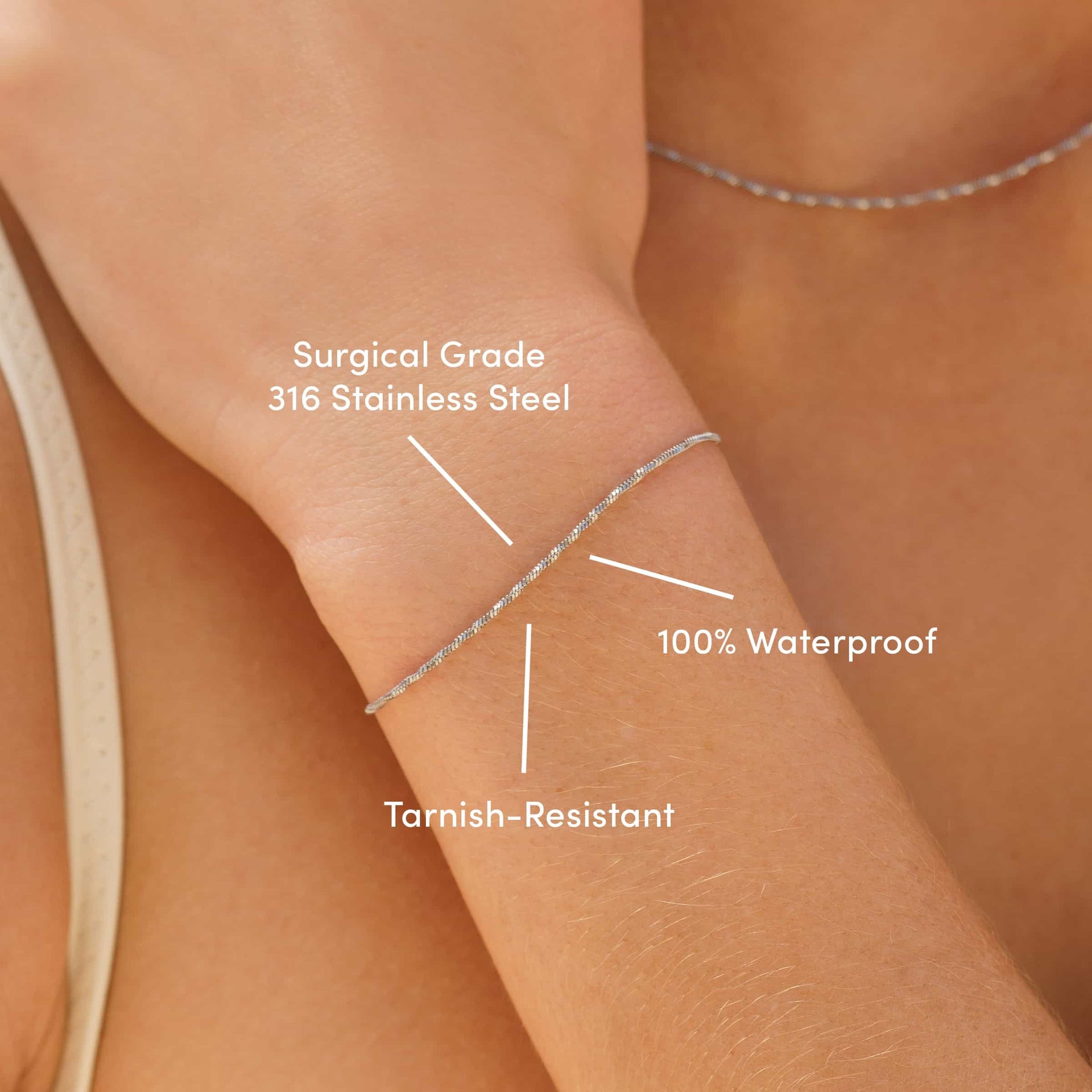 a close up of a dainty stainless steel snake chain bracelet worn by a model with the text overlayed "surgical grade 316 stainless steel, tarnish-resistant, & 100% waterproof"