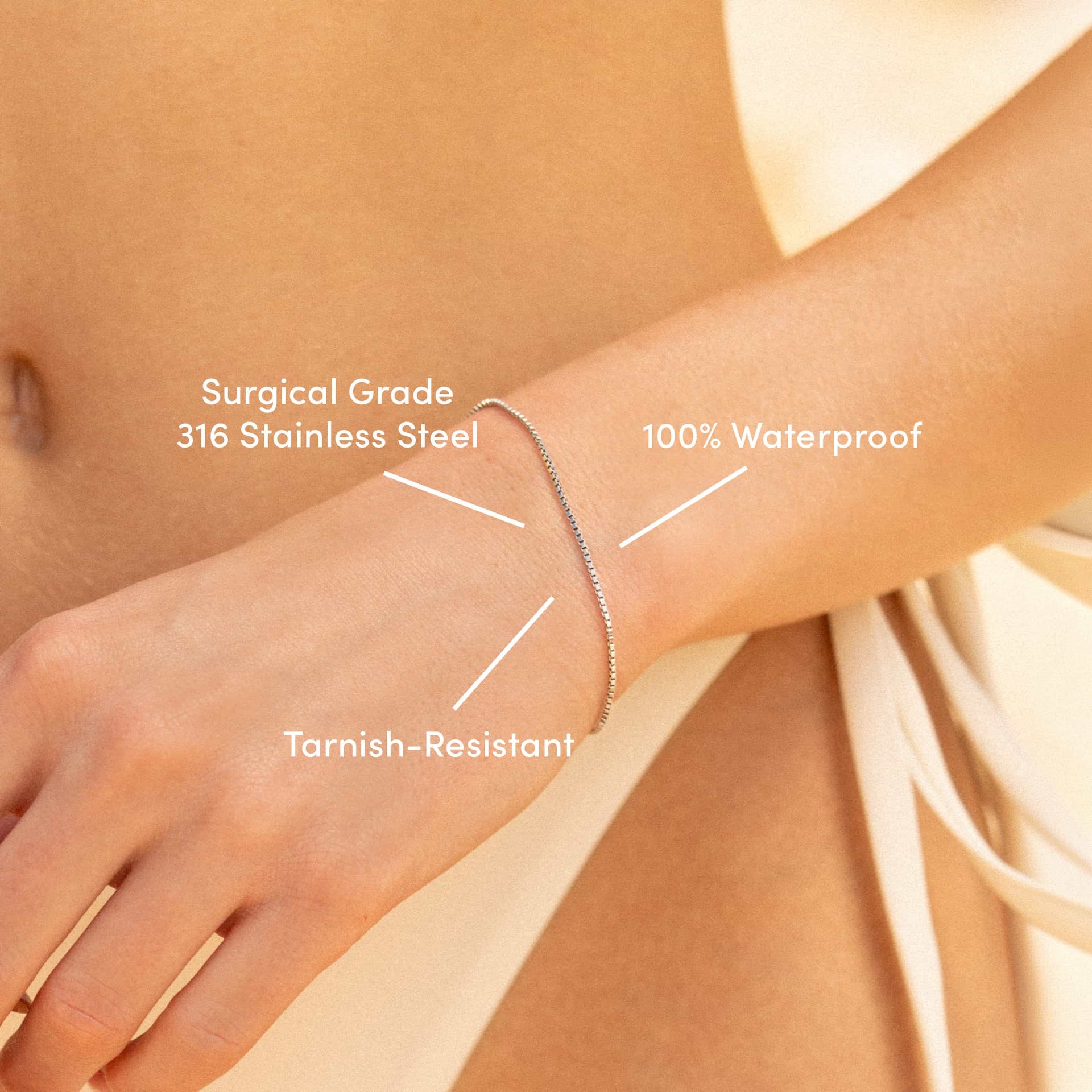 a close up of a simple stainless steel box chain bracelet on a model in an off white bikini with the text overlayed: "surgical grade 316 stainless steel, tarnish-resistant, 100% waterproof"