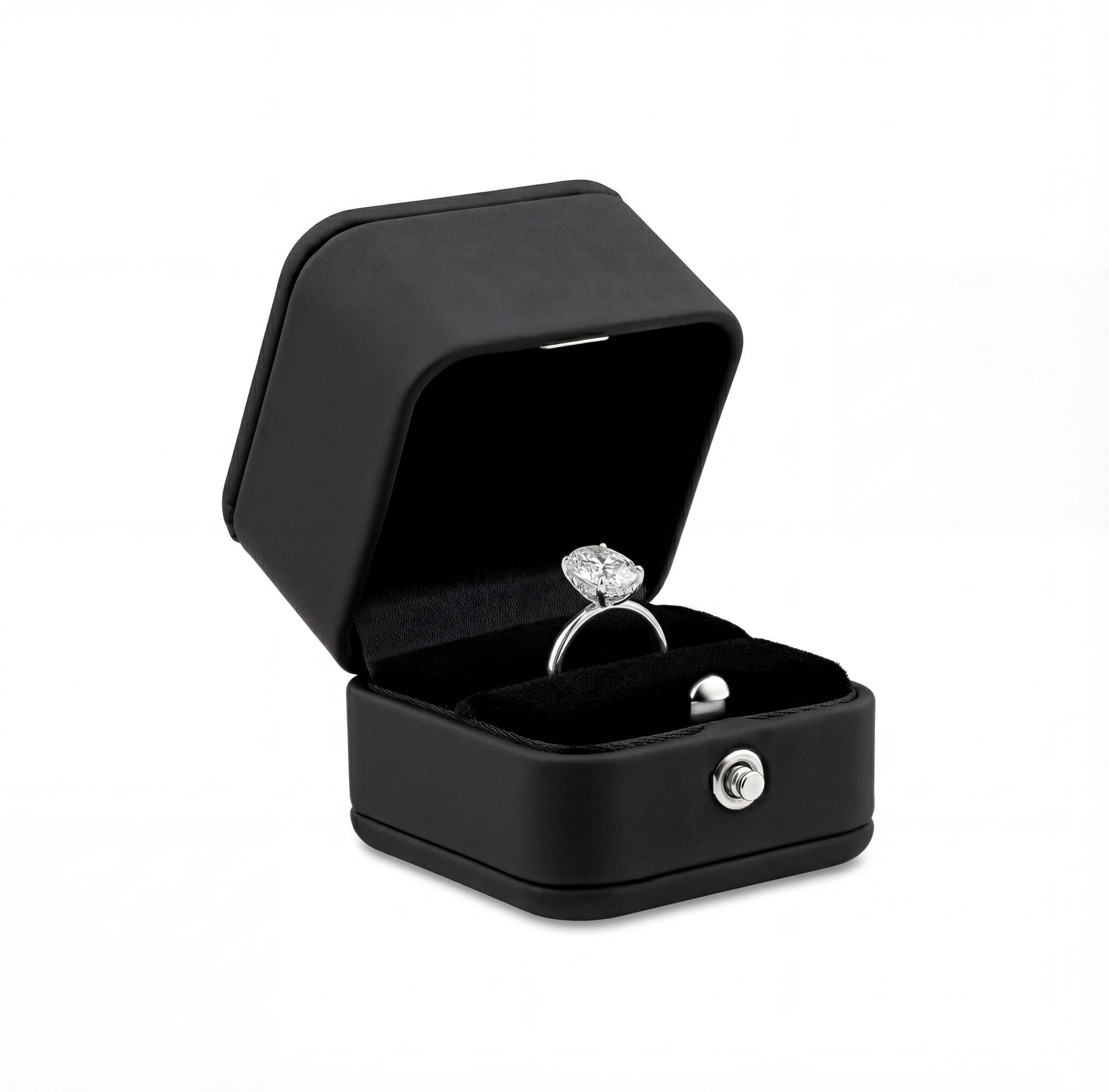 black synthetic leather ring box with black soft interior, a silver engagement ring inside, and a silver push-button detail on a white background