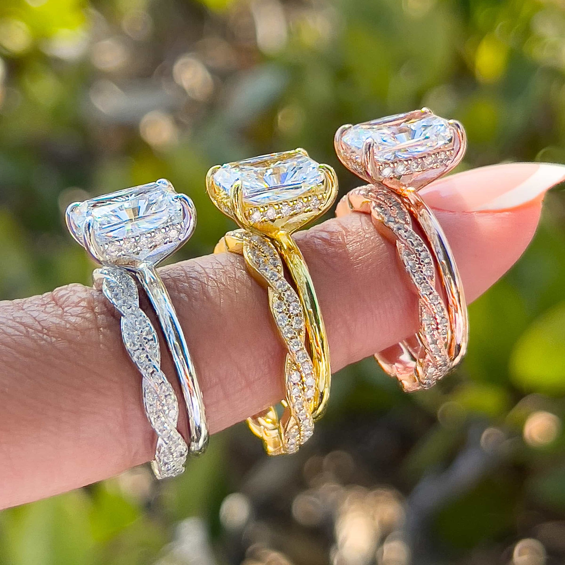 stunning 3 carat radiant cut wedding ring set shown in silver, gold, and rose gold on model with french tip nails in front of greenery