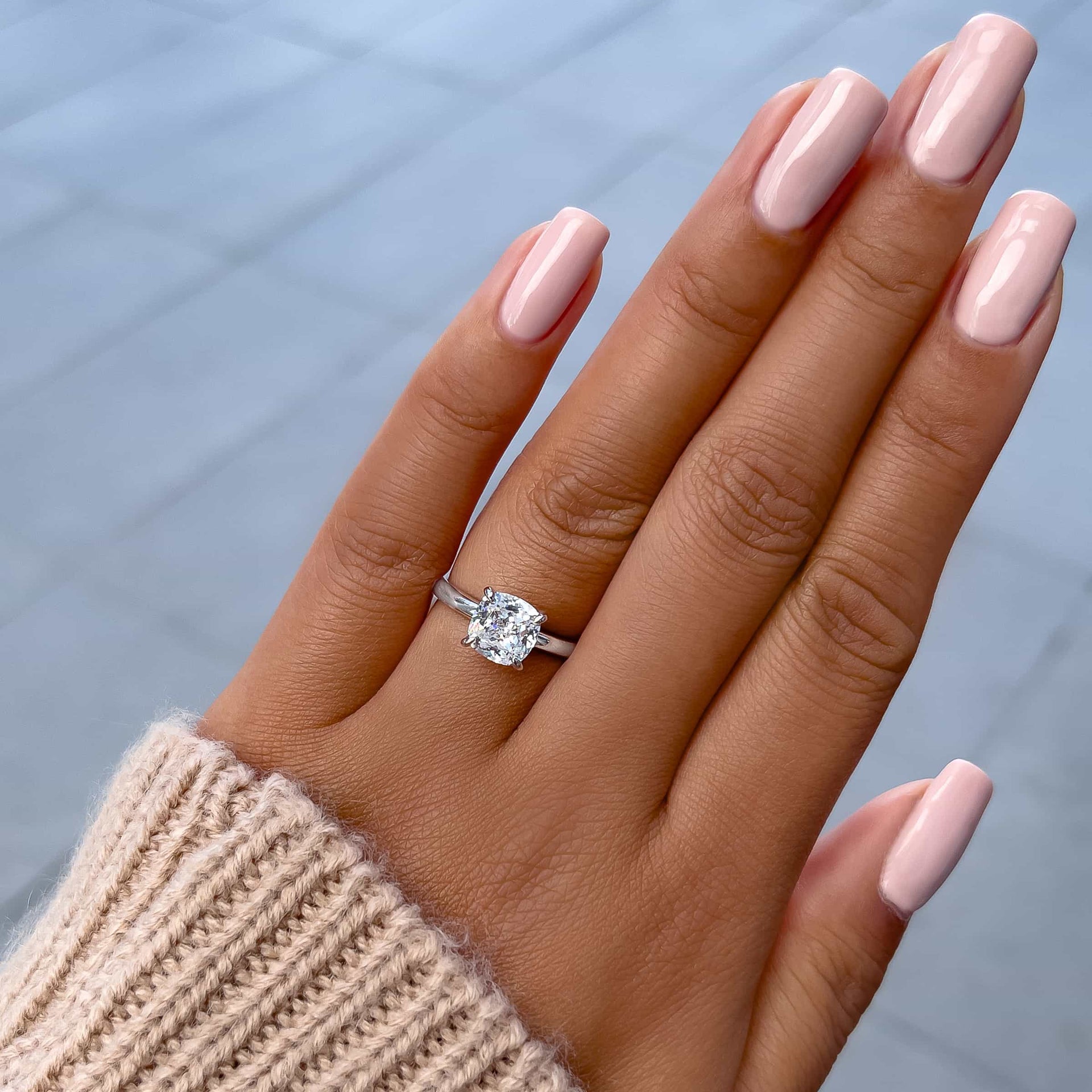 stunning silver 1.5 carat cushion cut engagement ring on model with light pink nails and tan sweater