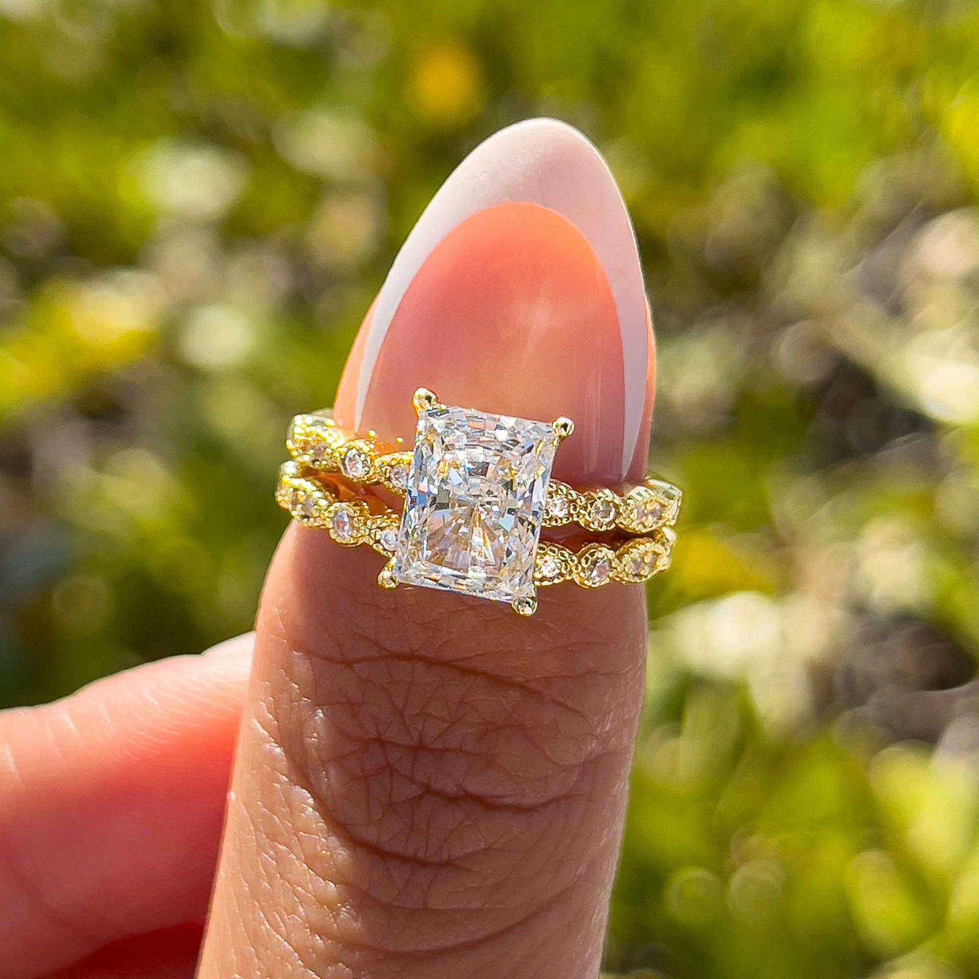 sparkling gold vintage 1.5 carat radiant cut half eternity wedding ring set on model with french tip nails in front of greenery