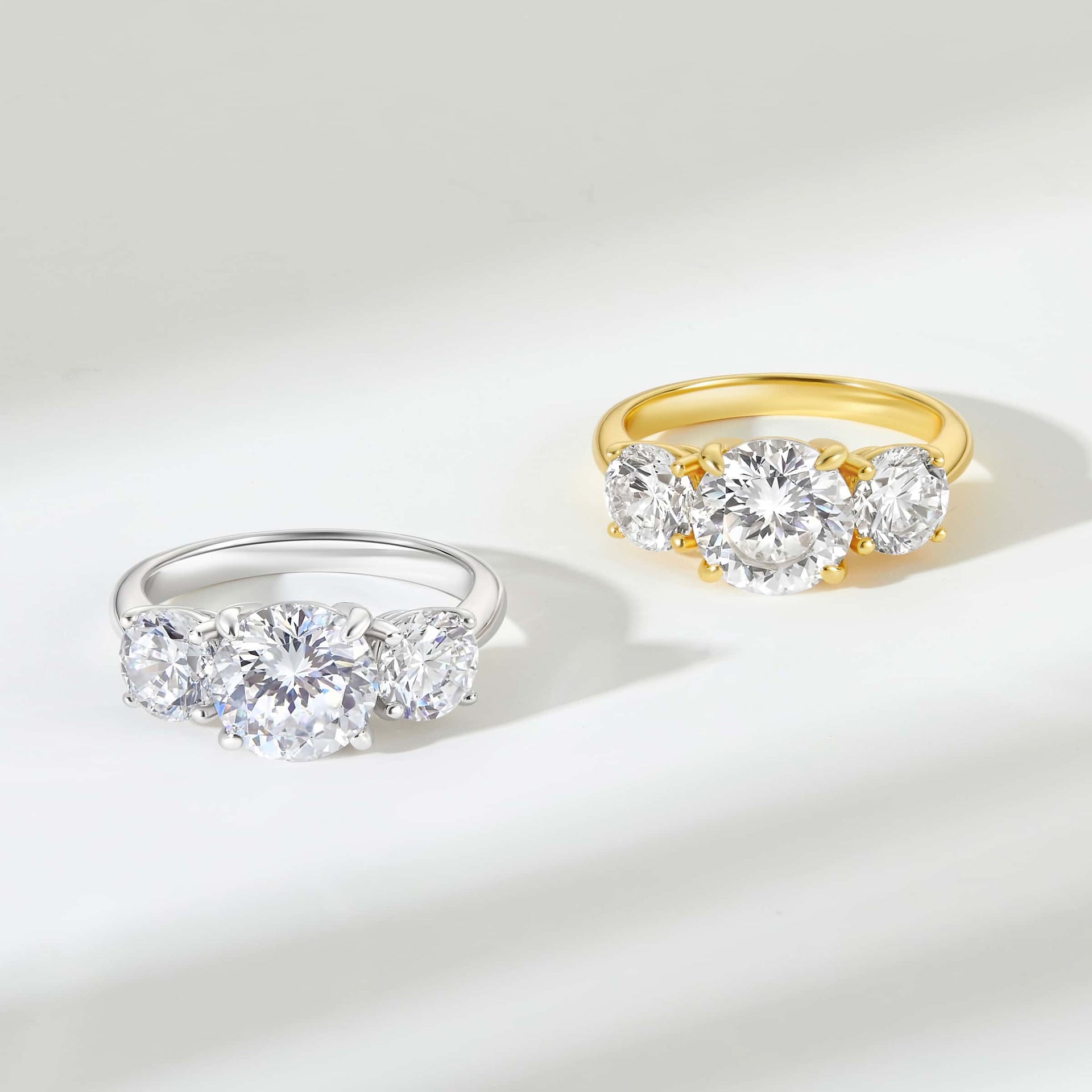 trinity round cut engagement rings shown in gold and silver on white background