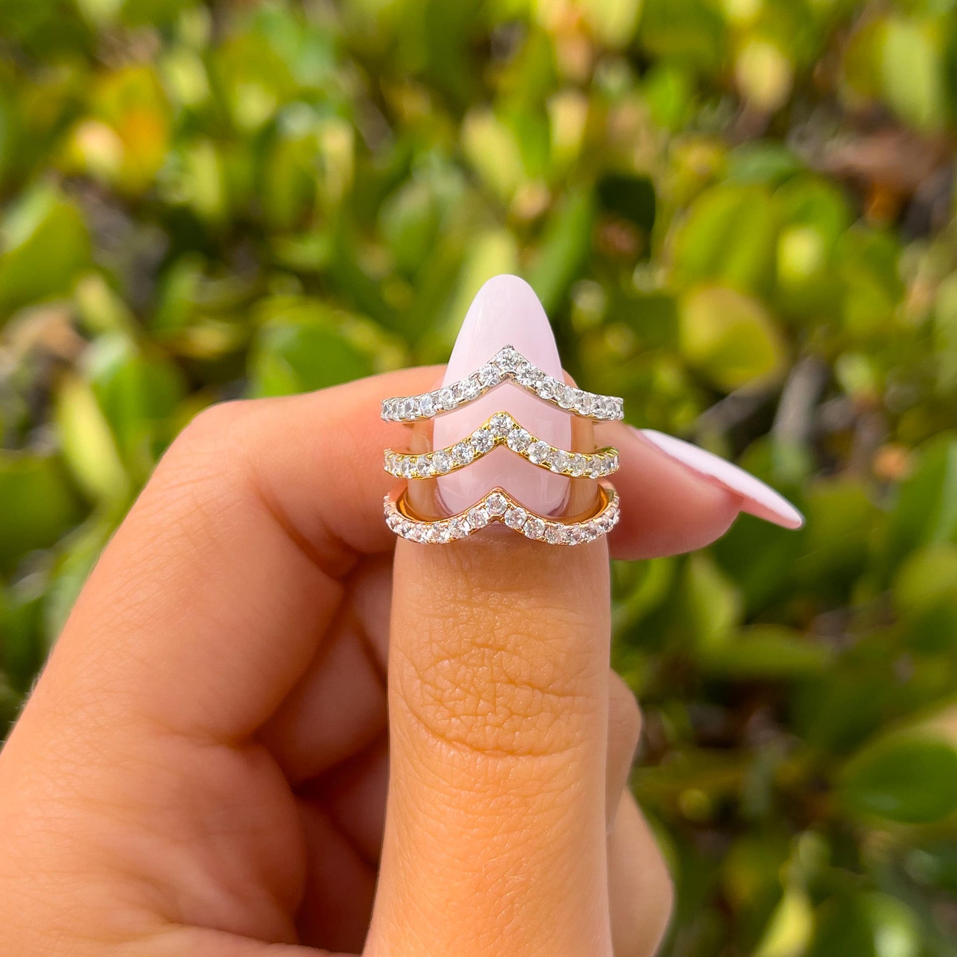 three chevron half eternity wedding bands shown in silver, gold, and rose gold held by model with light pink nails