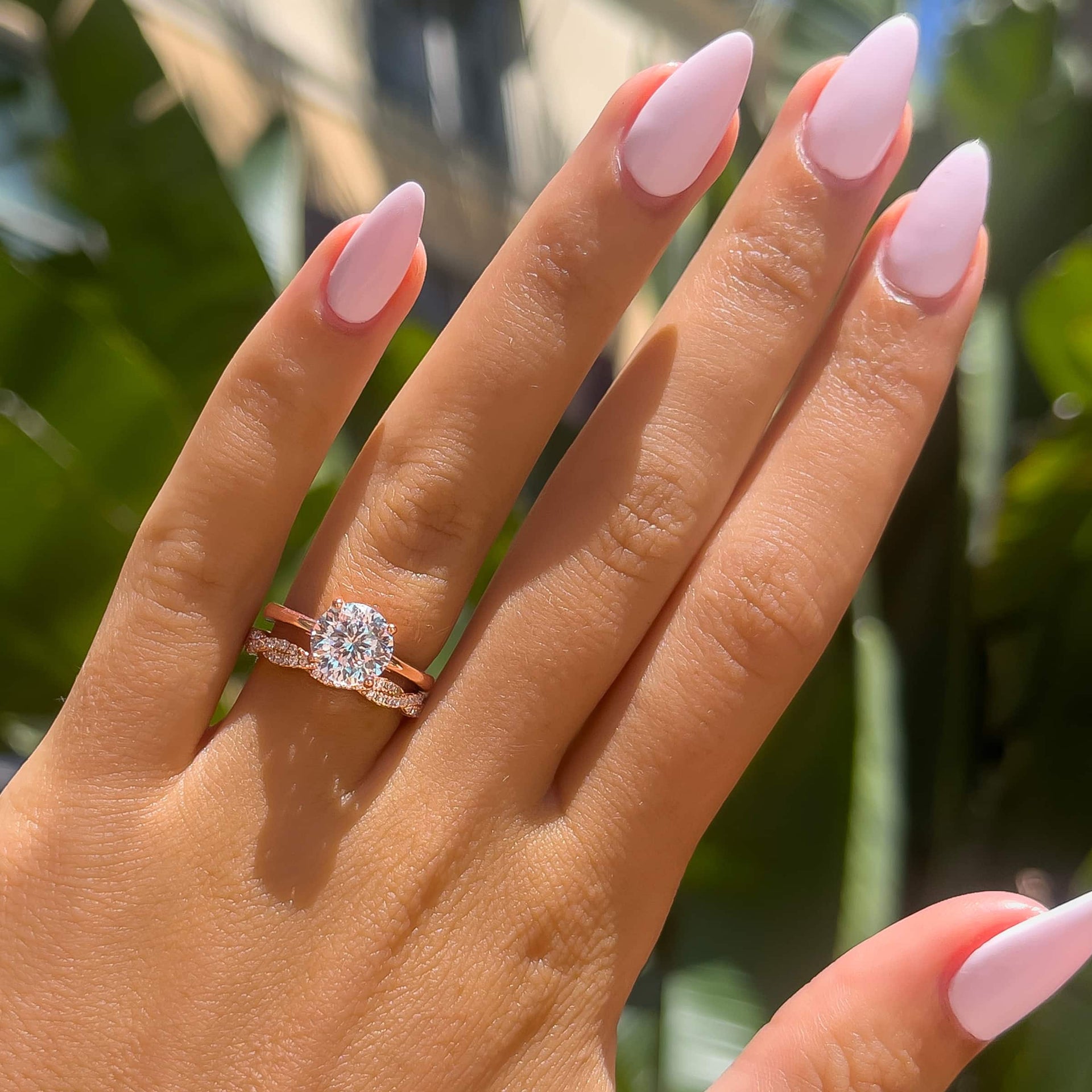 2 carat round cut solitaire engagement ring paired with twisting detail wedding band on model with light pink nails