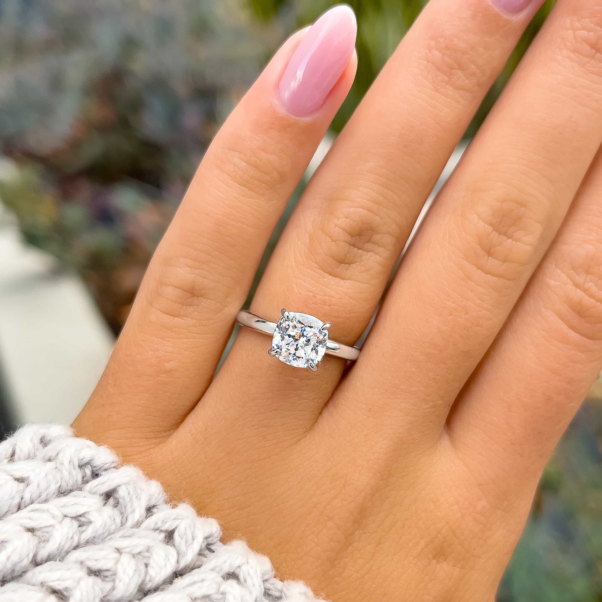 simple silver cushion cut solitaire ring on model with light pink nails and neutral knit sweater