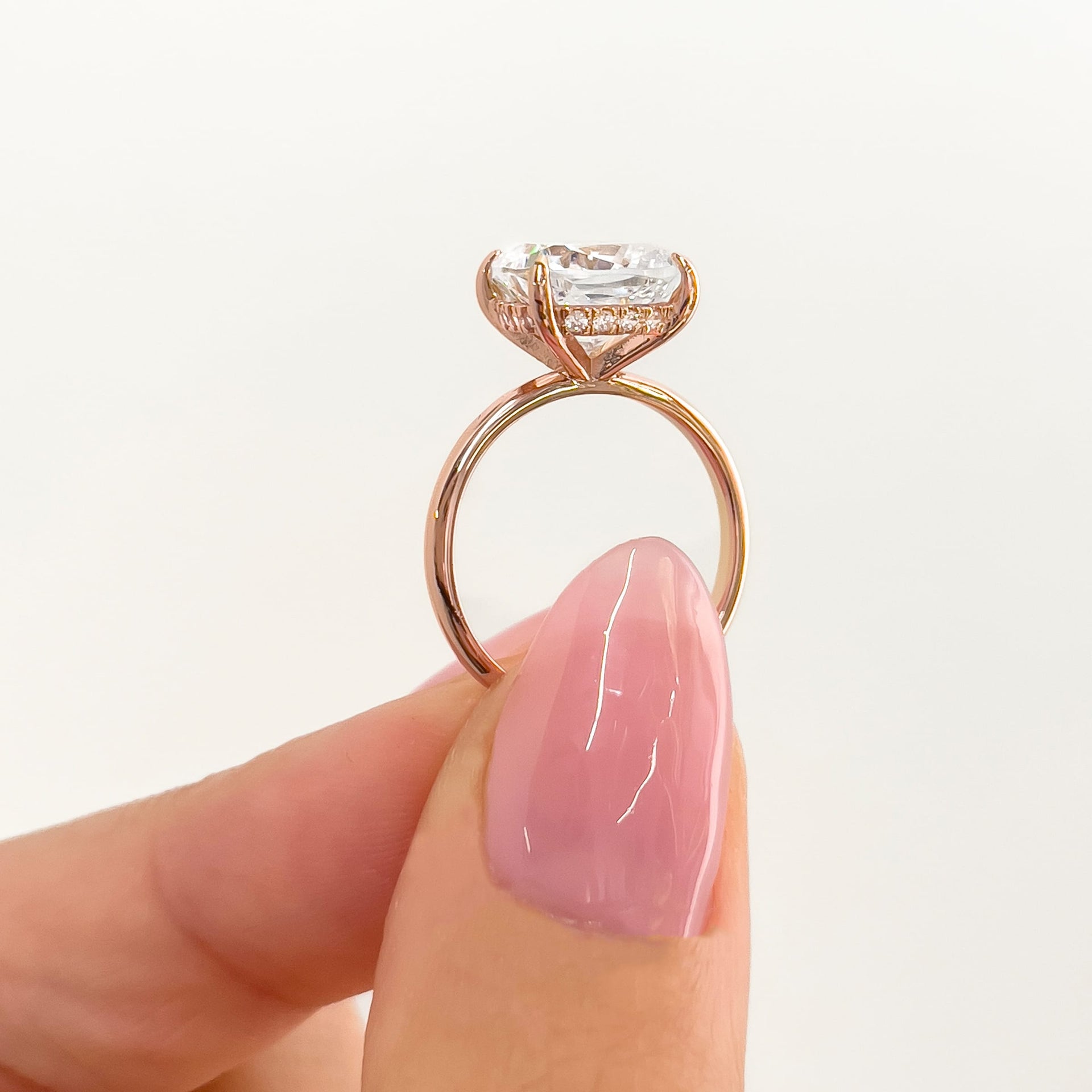 setting shot of rose gold cushion cut solitaire held by model with pink nails