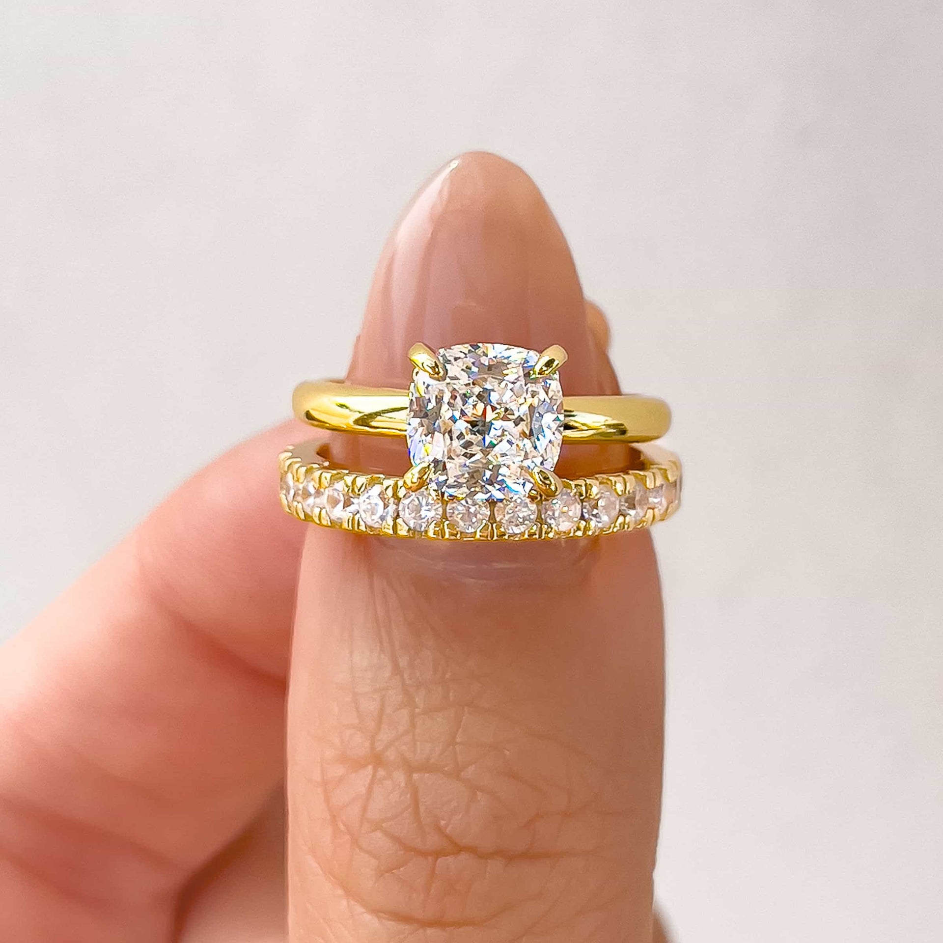 classic gold wedding ring set made up of a 1.5 carat cushion cut solitaire engagement ring and full eternity wedding band held by model with neutral nails