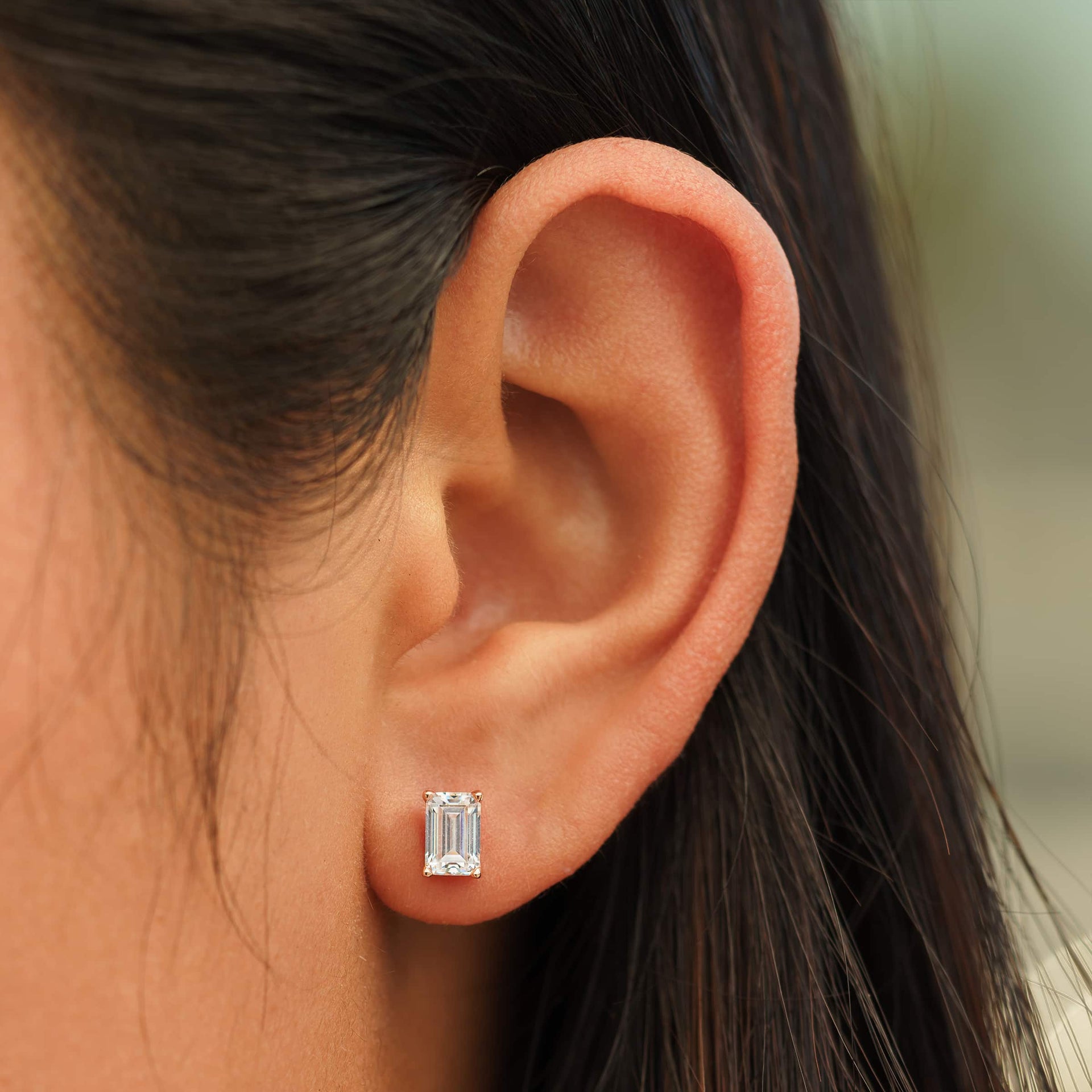 small rose gold emerald cut stud earrings on female model