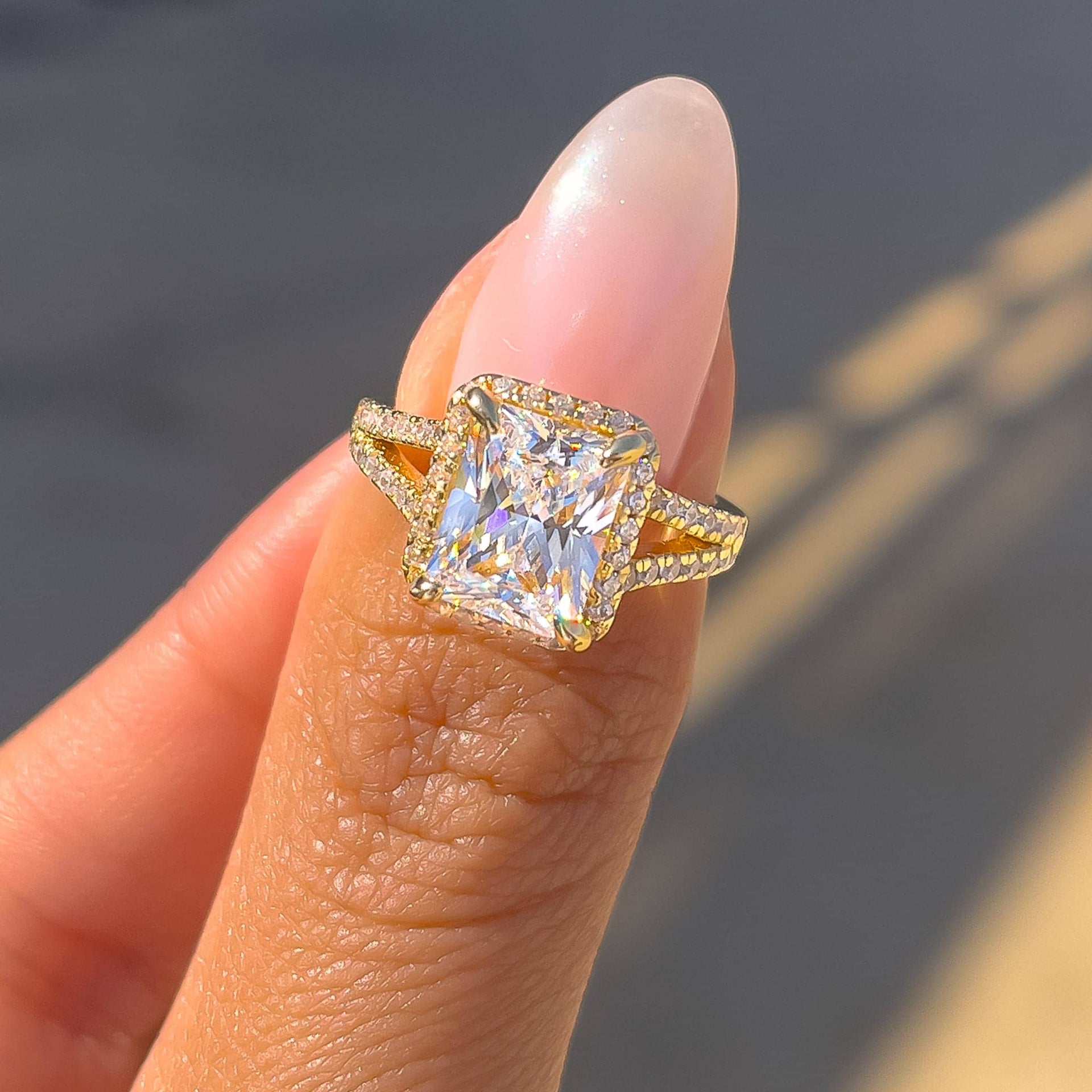 gold radiant cut engagement ring on models thumb with pink nail