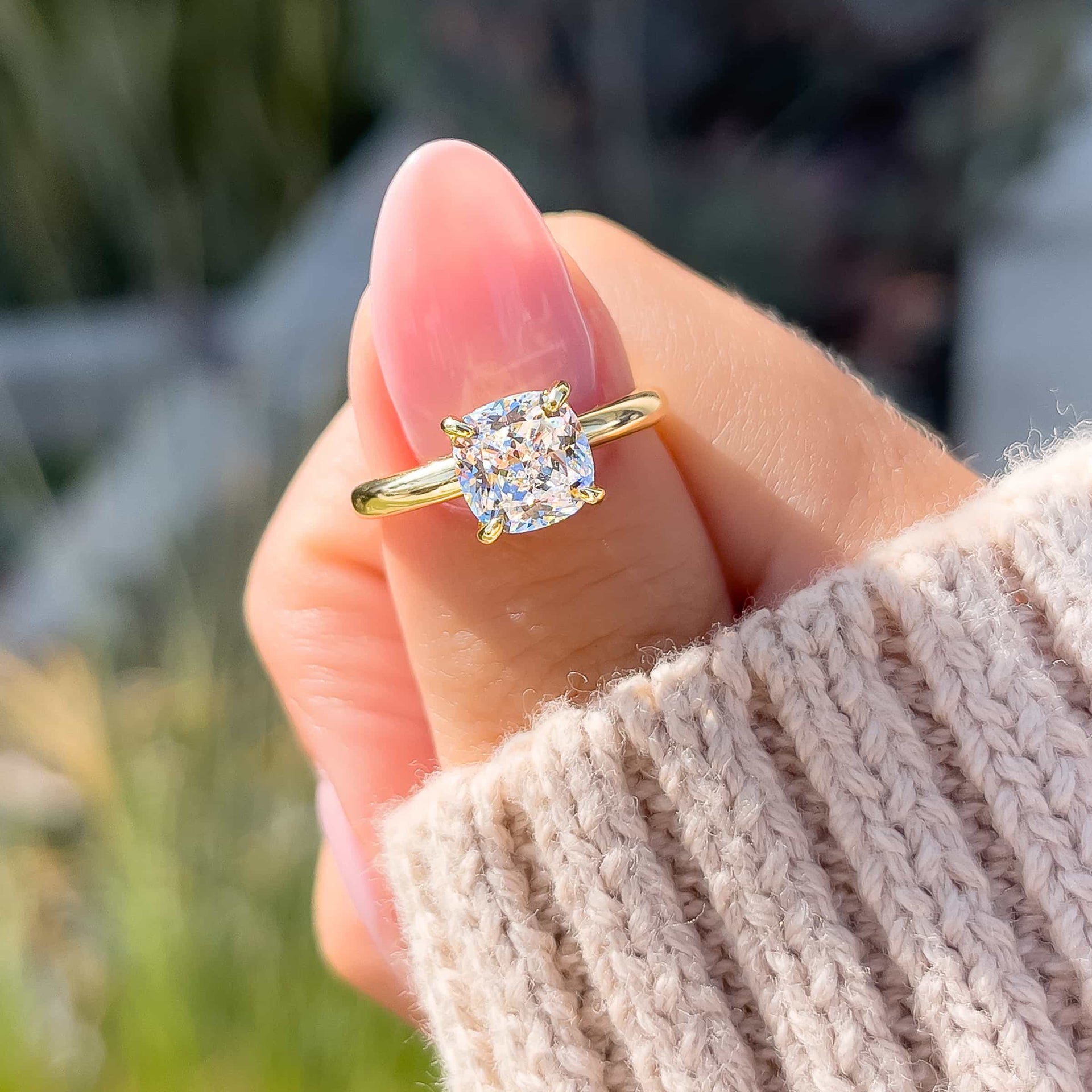 gold petite 1.5 carat cushion cut solitaire engagement ring shown on female model wearing tan sweater with light pink nails