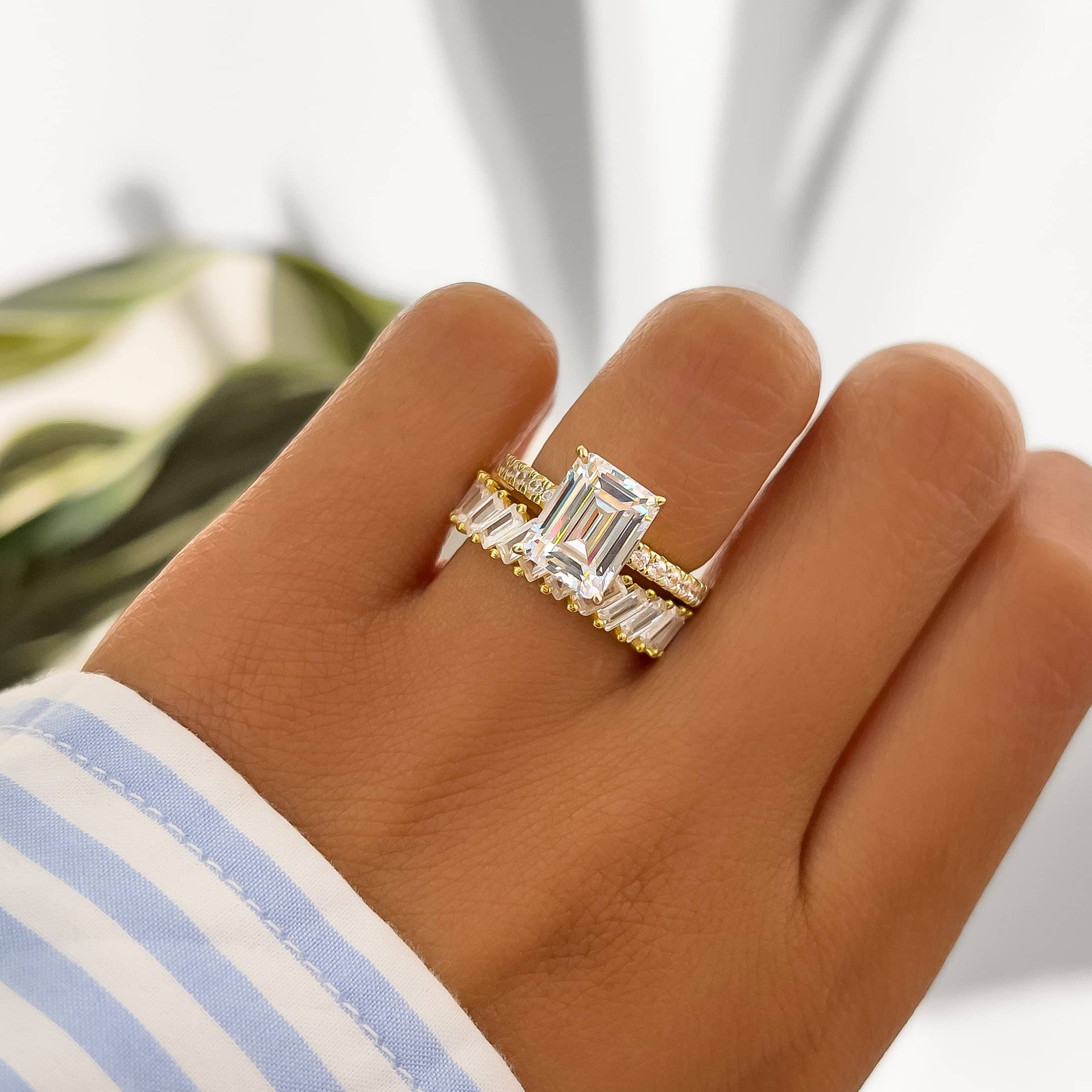 a gorgeous gold ring stack made up of an emerald cut engagement ring and a baguette style wedding band on model with striped top