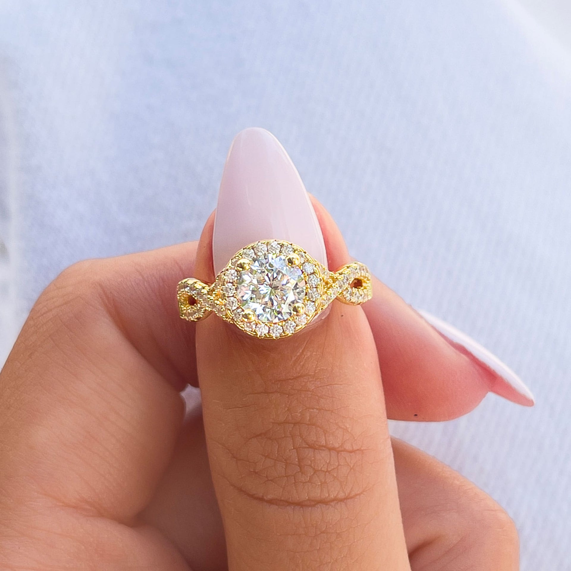 gold round cut vintage ring with halo and twisting detail on a model with light pink nails