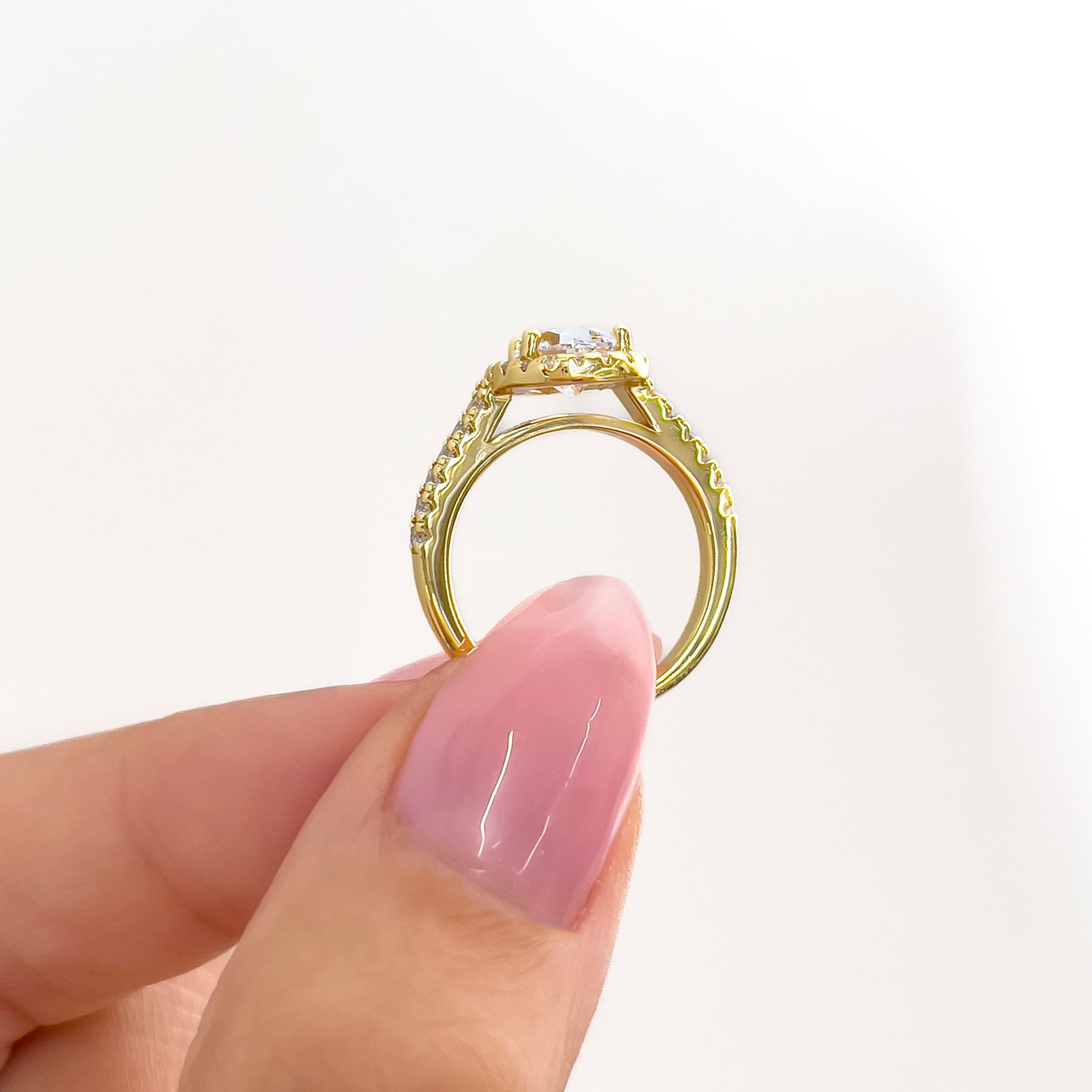 gold setting shot of pear cut halo half eternity engagement ring held by model with pink nails