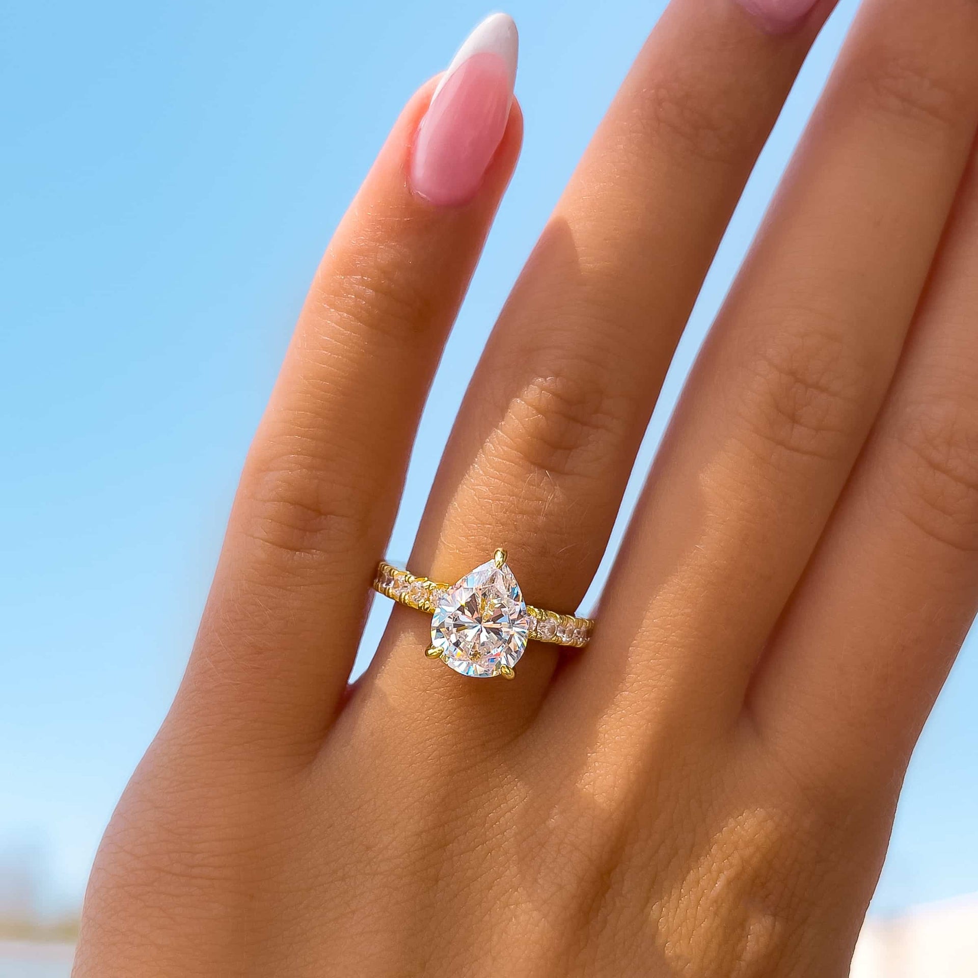 model with french tip nails wearing 3 carat pear cut engagement ring in gold