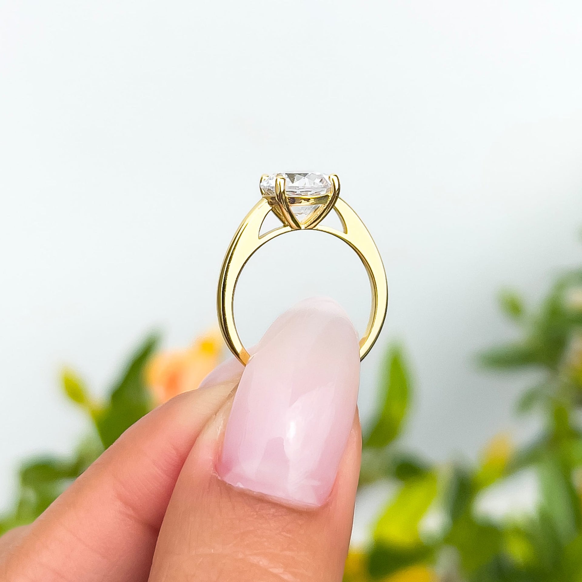 side view of 2 carat gold round cut solitaire engagement ring held by model with neutral nail