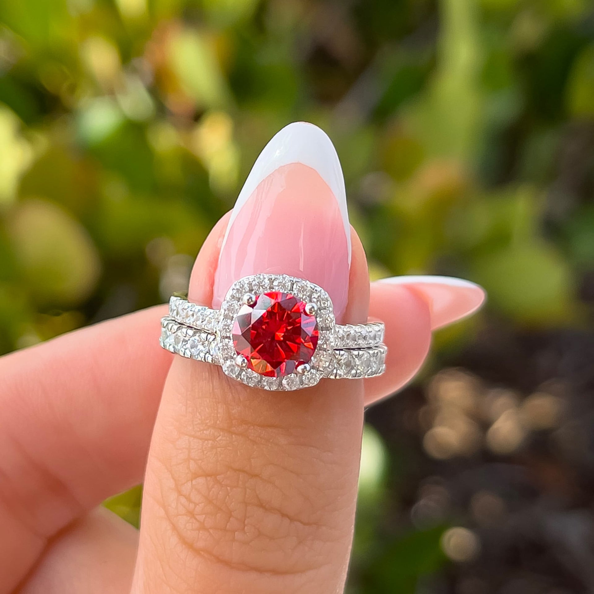 unique colored ruby gemstone halo engagement ring with silver wedding band on hand with french tip nails