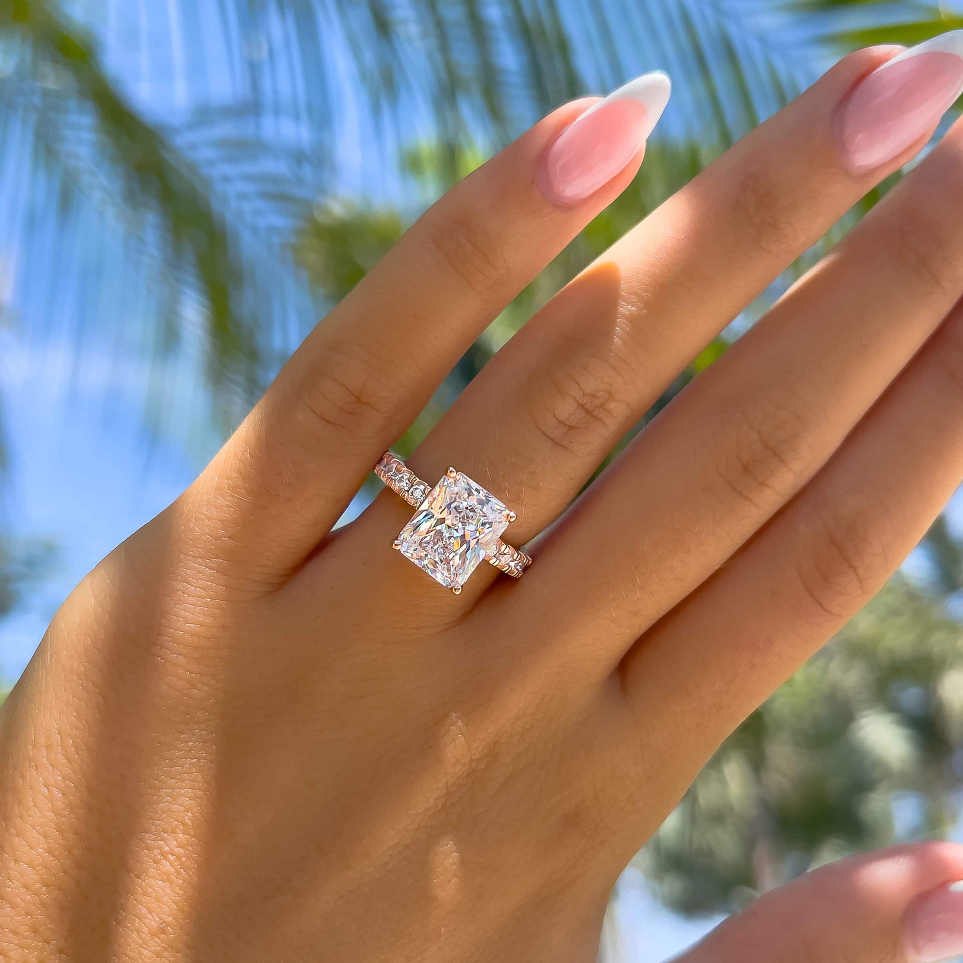 bold rose gold radiant cut engagement ring with half eternity band detailing on model with french tip nails