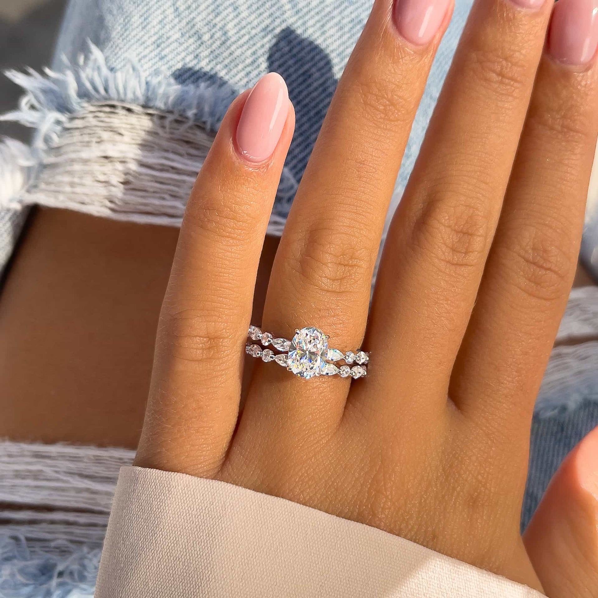 woman wearing gorgeous silver oval cut engagement ring paired with a sparkling half eternity band with jeans in background