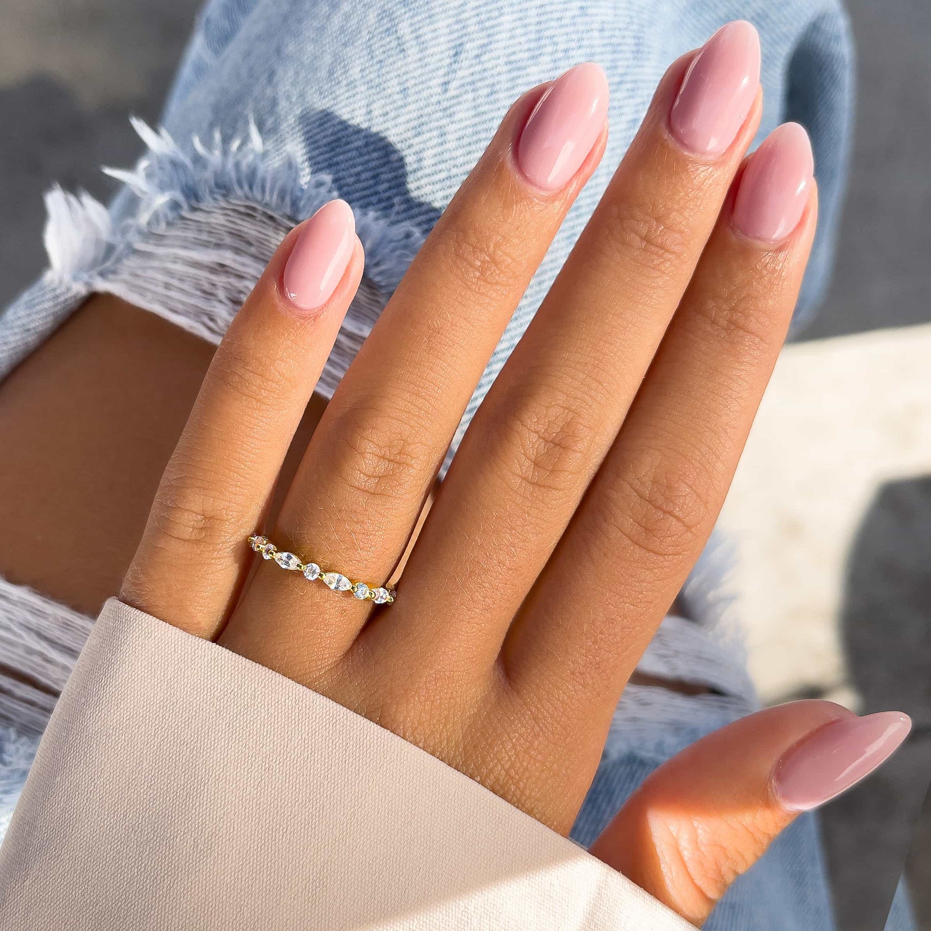 gold pave wedding band on model with pink nails and tan sleeve with blue jeans 