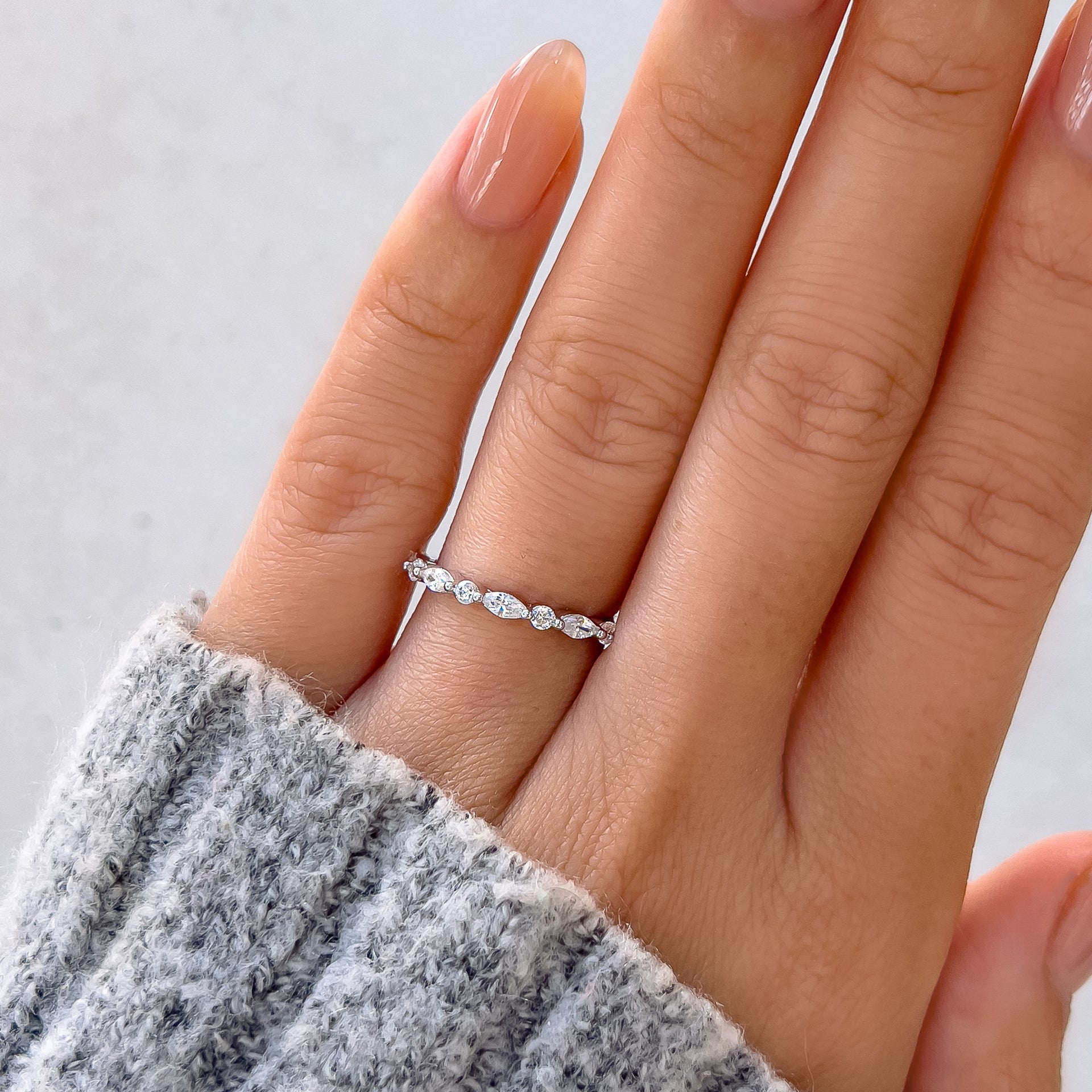 silver wedding band on model hand with gray sweater and gray background