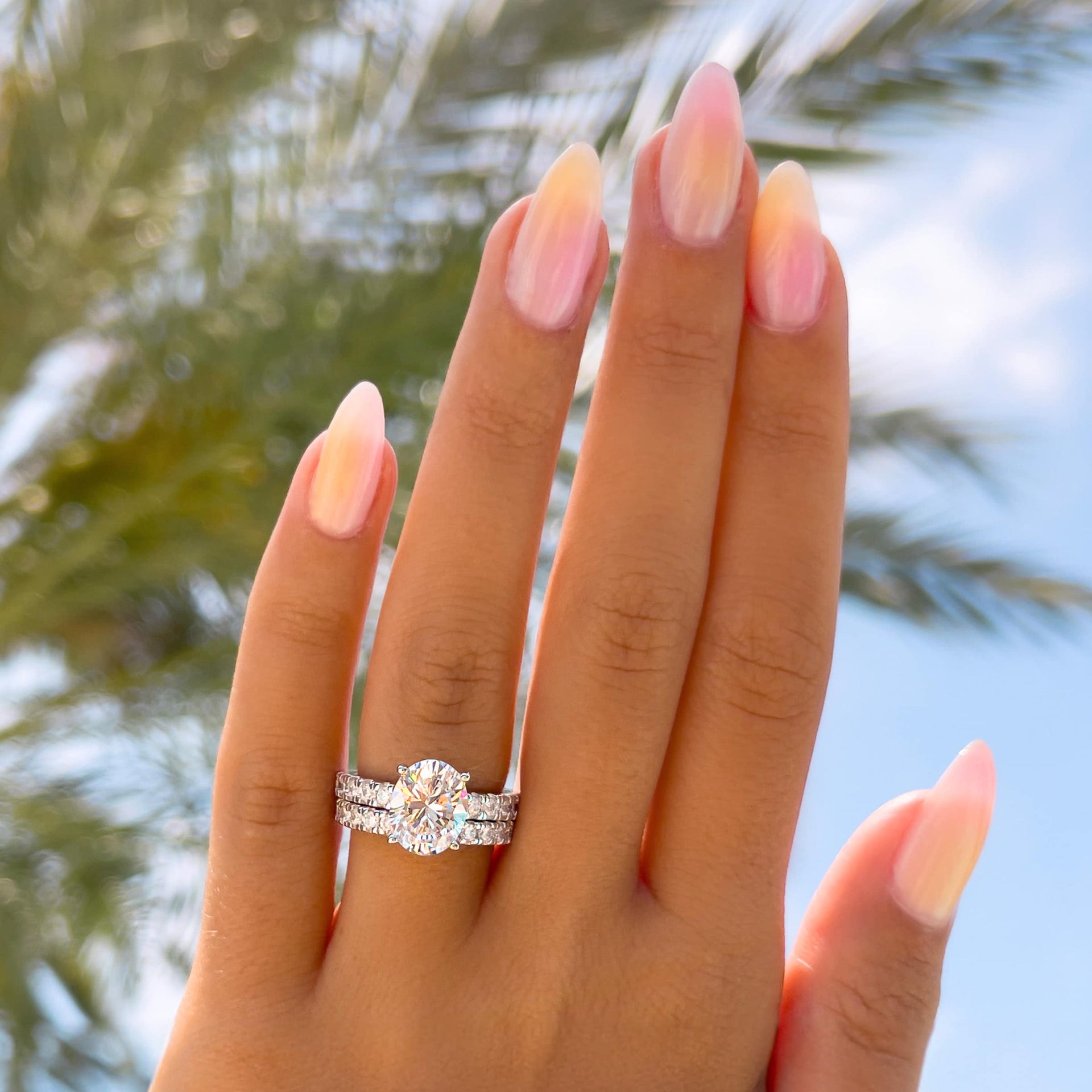 stunning 3 carat silver oval cut engagement ring with matching silver wedding band with palm tree in the background