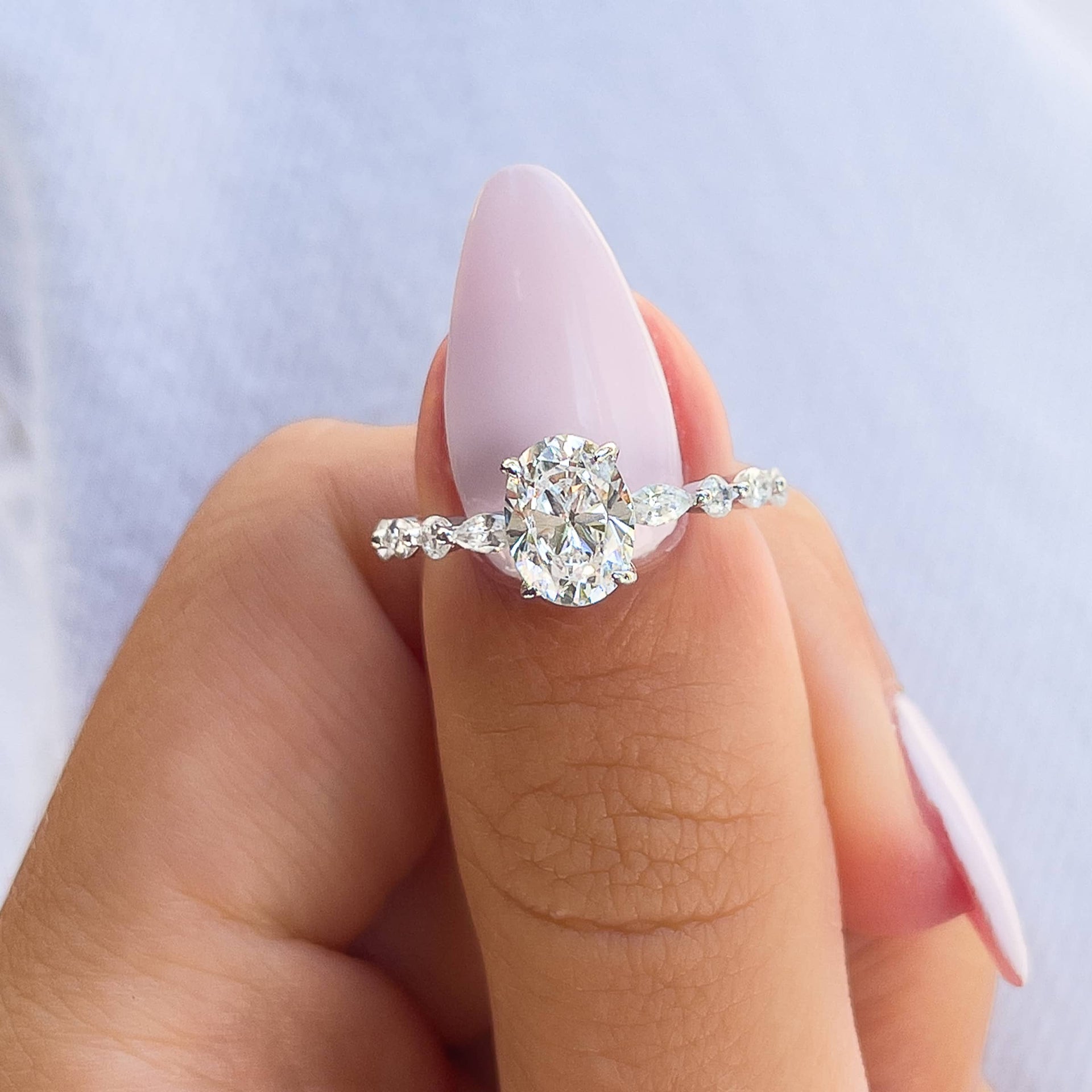 woman pinching silver oval cut engagement ring on thumb with pink nails