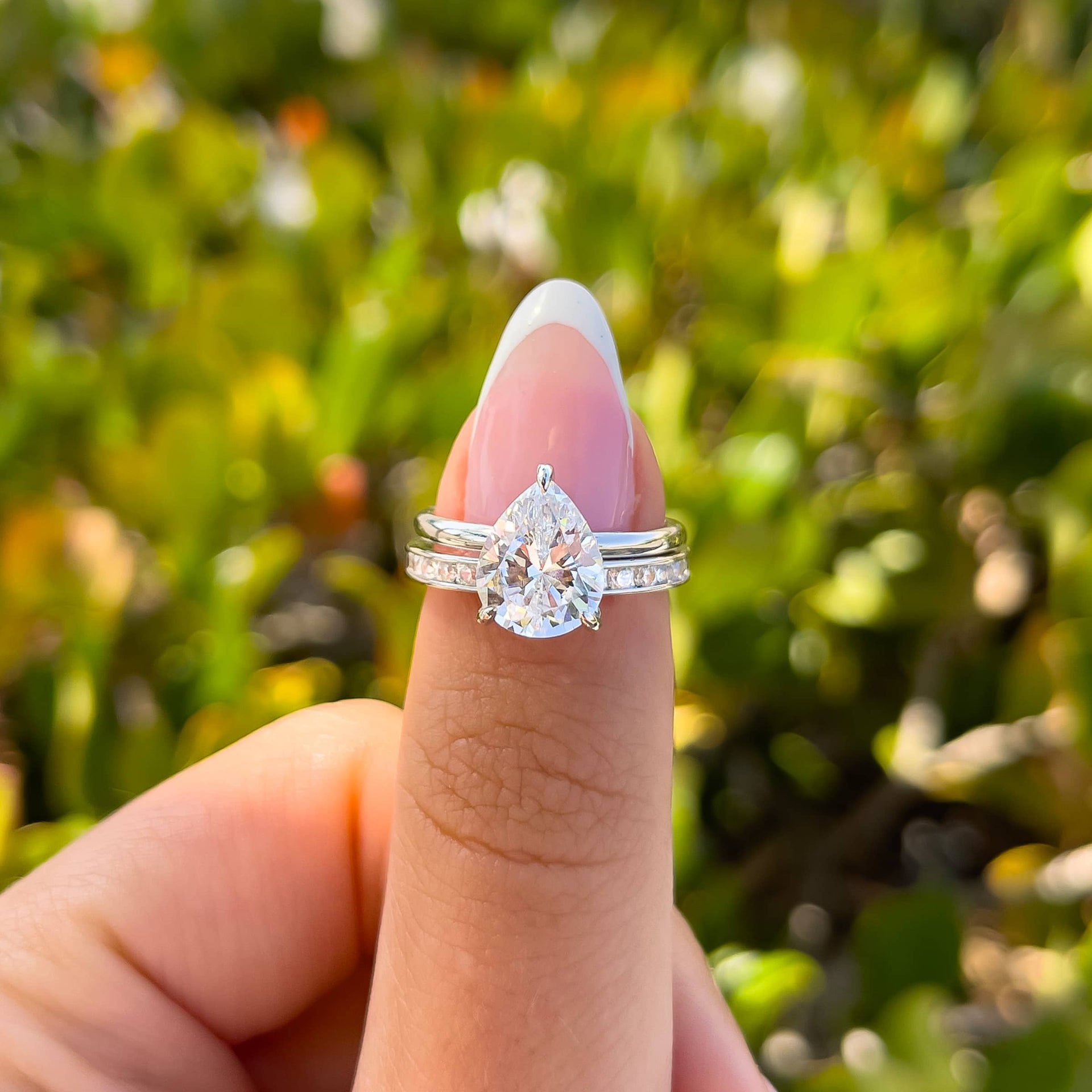 silver 3 carat pear cut solitaire engagement ring with unique silver wedding band on model with french tip nails