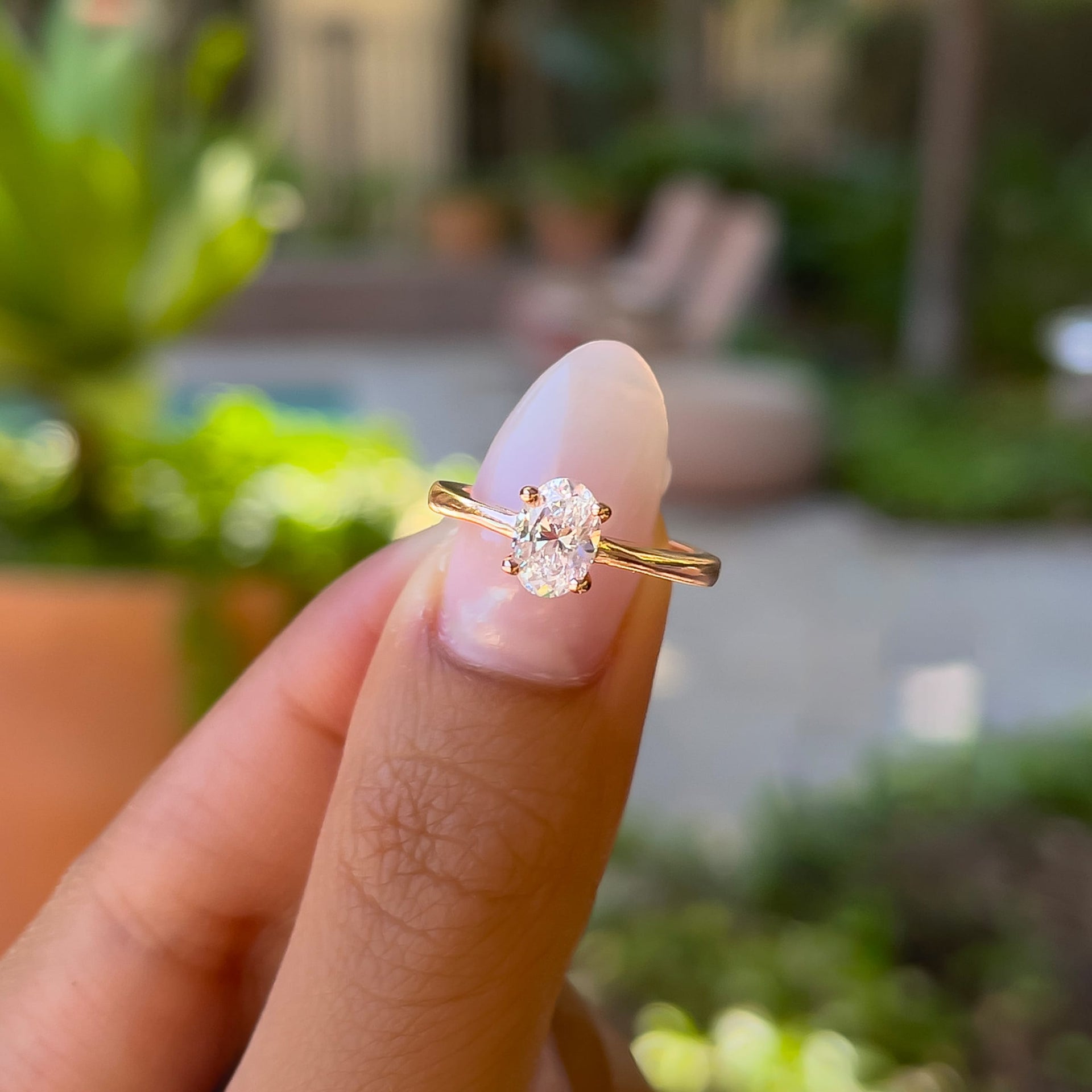 petite rose gold 1 carat oval cut solitaire engagement ring held by model with neutral nails