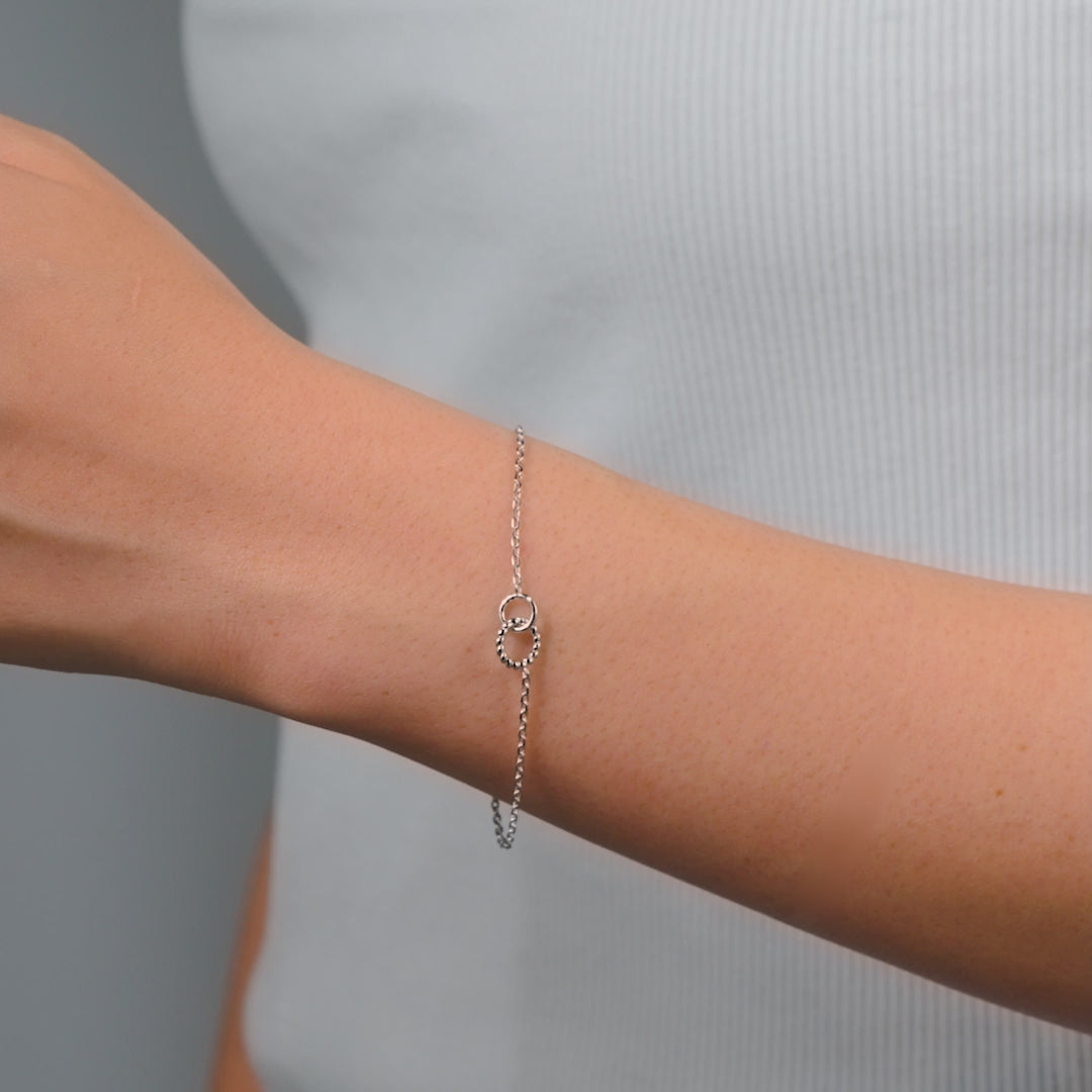 video of dainty silver bracelet with minimal interlocking hoop detail held by model with light pink nails
