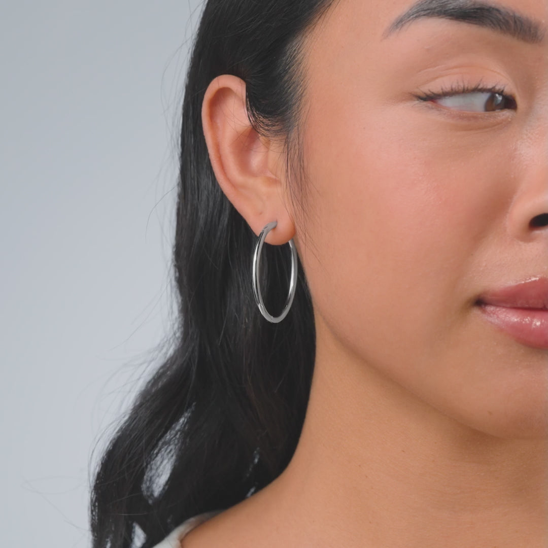 a video of simple silver hoops worn by a model with dark hair