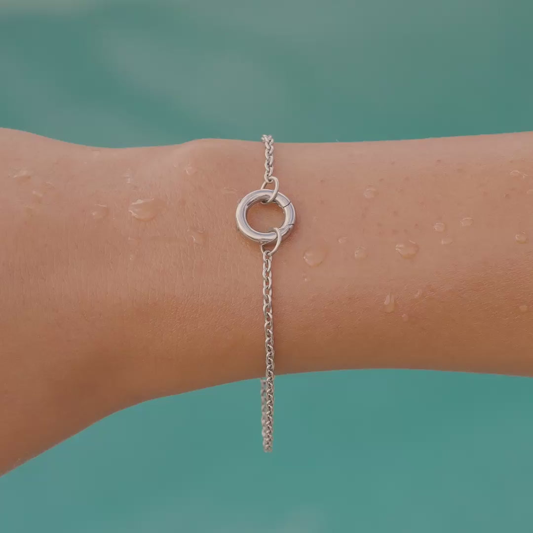 video of a silver stainless steel charm bracelet on a model by the pool