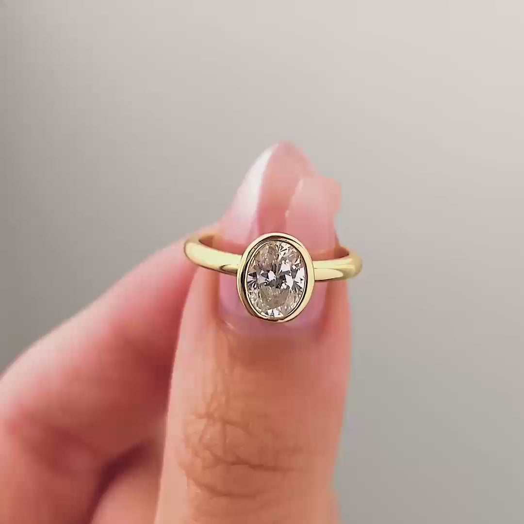 a video compilation of a gold oval cut bezel engagement ring shown in different settings by a model with pink manicured nails