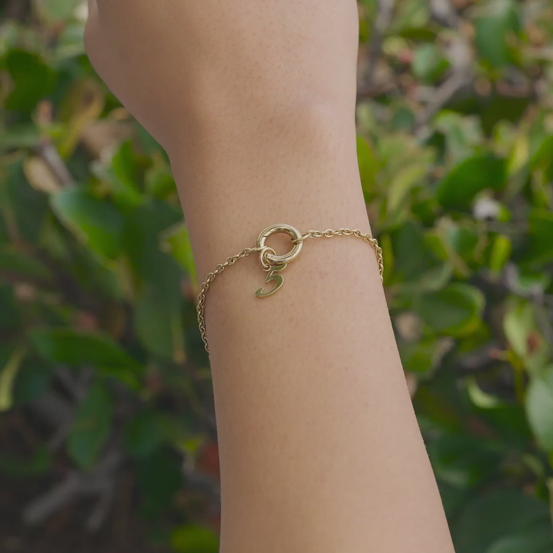 Gold Stainless Steel Charm Bracelet with Gold Number Charm in "5" worn by model who is outside