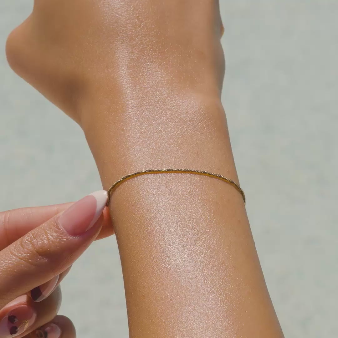 a video of a 14k gold PVD plated stainless steel dainty snake chain bracelet on a model with french tip nails by the pool