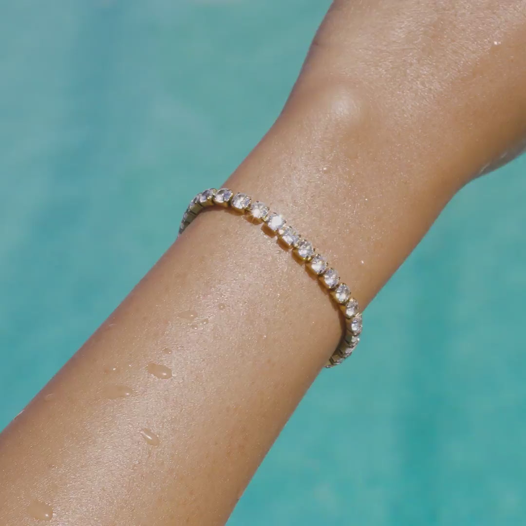 video of a stunning, waterproof, 14k gold PVD plated stainless steel tennis bracelet on a model by the pool