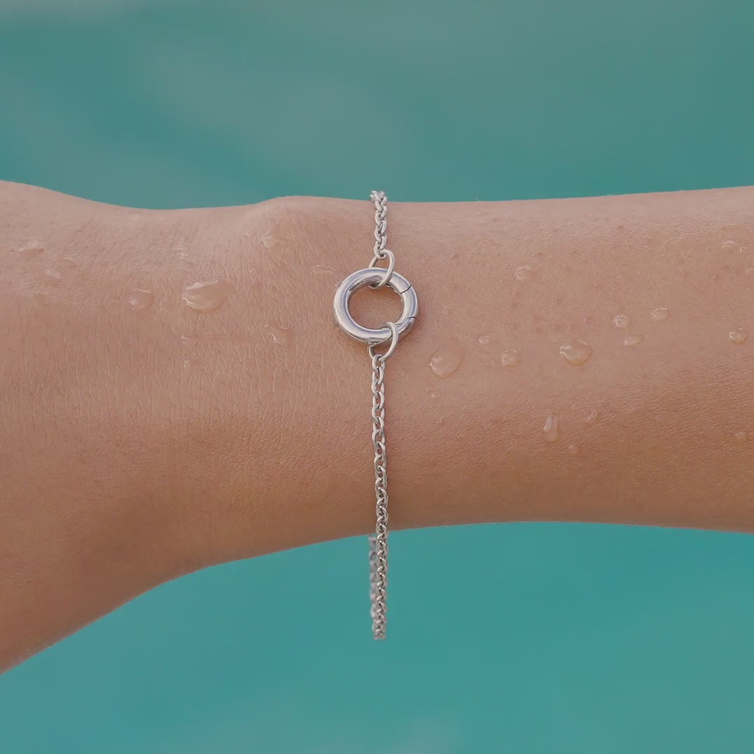 video of a silver stainless steel charm bracelet on a model by the pool