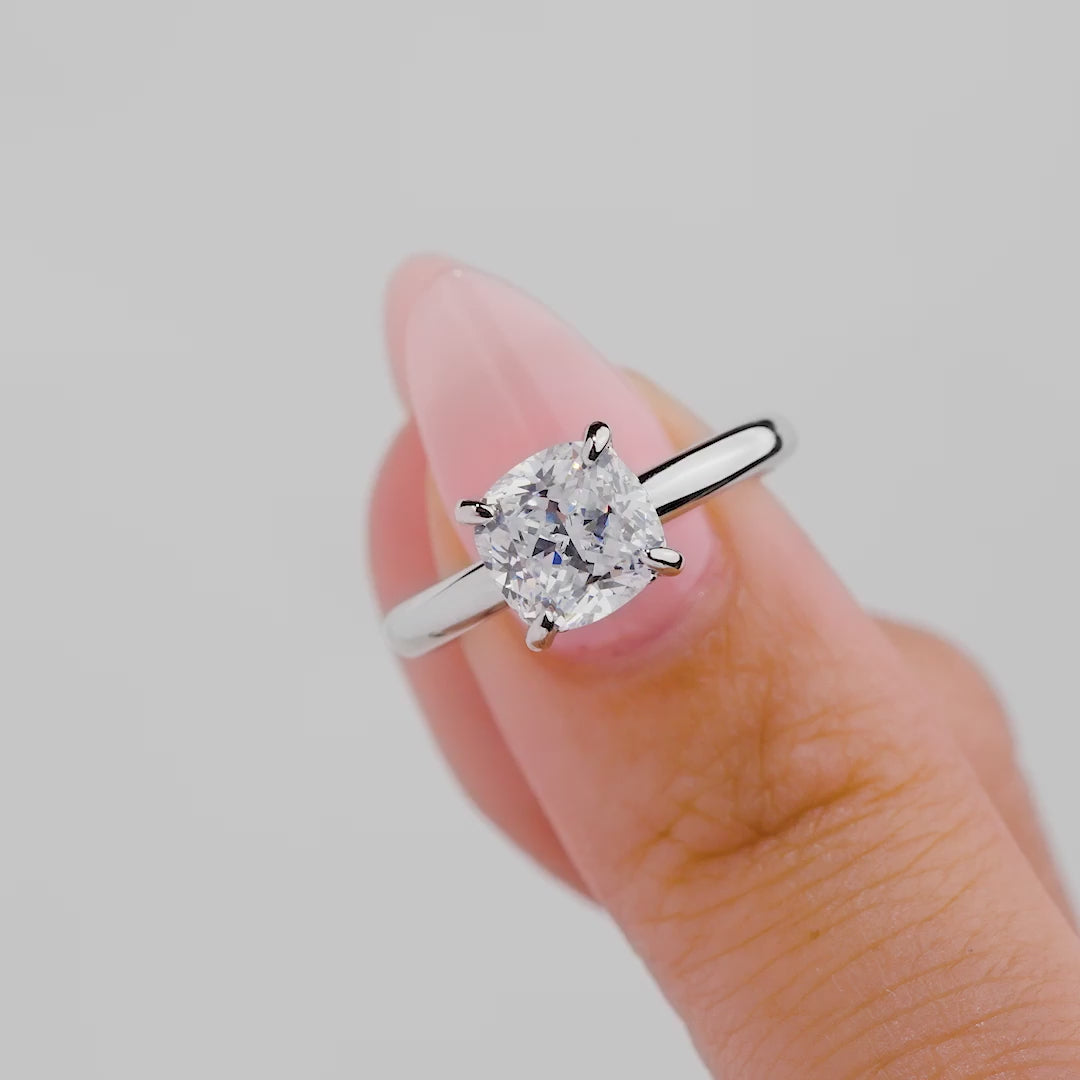 video of classic 1.5 carat cushion cut solitaire engagement ring with hidden halo detail held by model with light pink nails