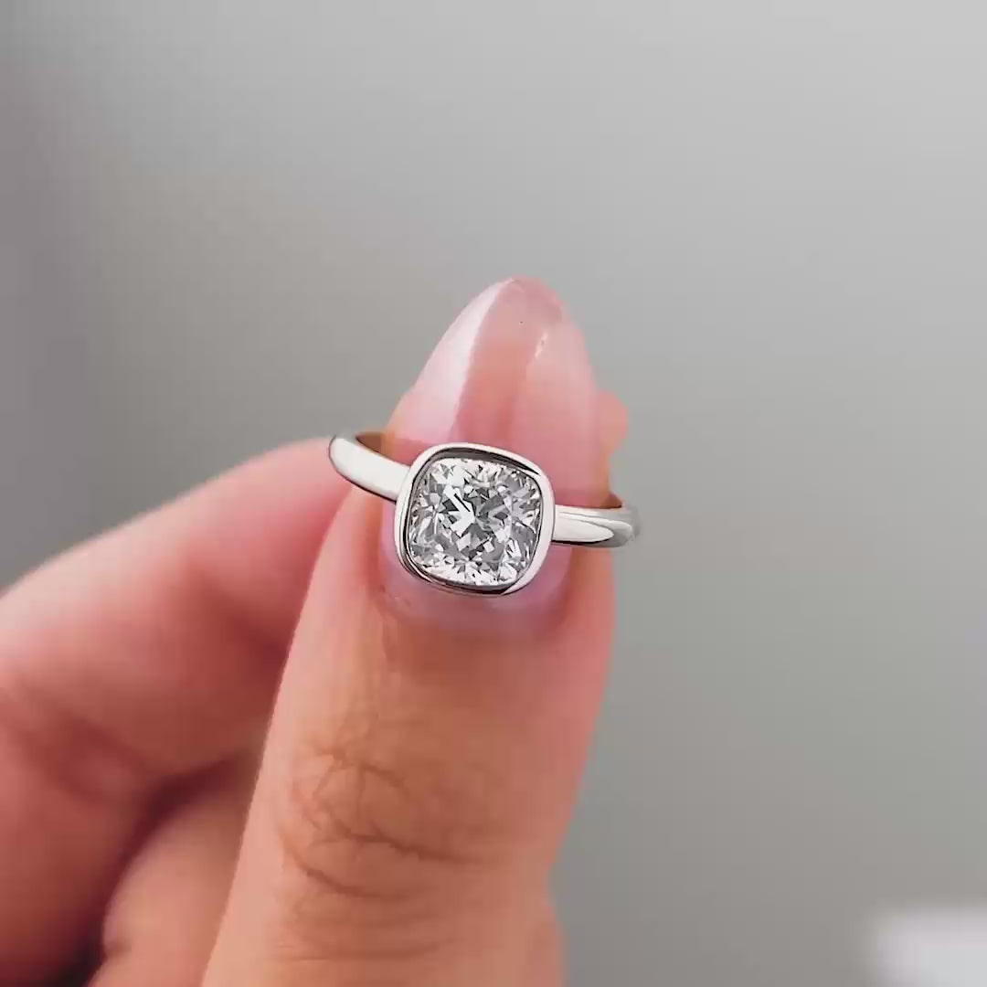 a video compilation of a silver cushion cut bezel engagement ring shown in different settings by a model with pink manicured nails