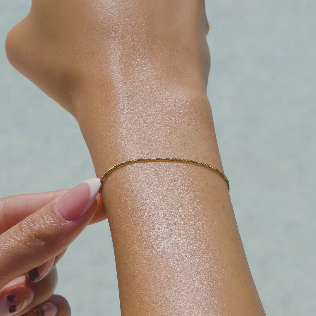 a video of a 14k gold PVD plated stainless steel dainty snake chain bracelet on a model with french tip nails by the pool