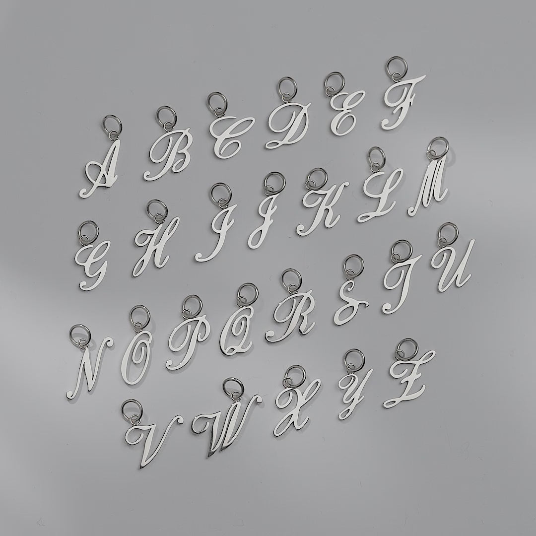 video of silver stainless steel cursive letter charms shown in A-Z on an off white background, with the "D" charm shown worn on a silver charm necklace and bracelet, both on a model