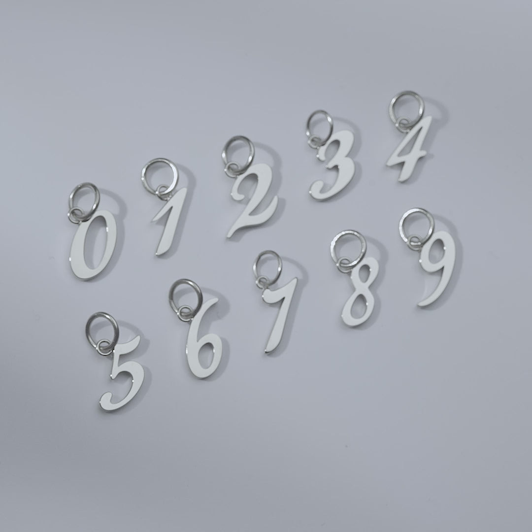 video of silver stainless steel number charms 0-9 shown in flatlay version and attached to a charm necklace and bracelet