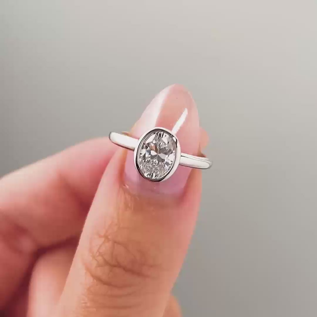 a video compilation of a silver oval cut bezel engagement ring shown in different settings by a model with pink manicured nails