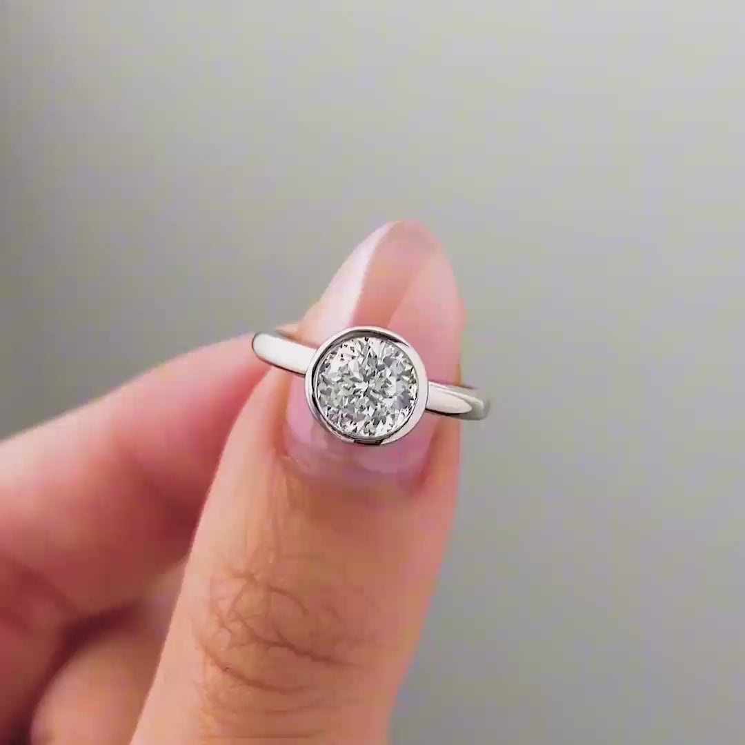 a video compilation of a silver round cut bezel engagement ring shown in different settings by a model with pink manicured nails