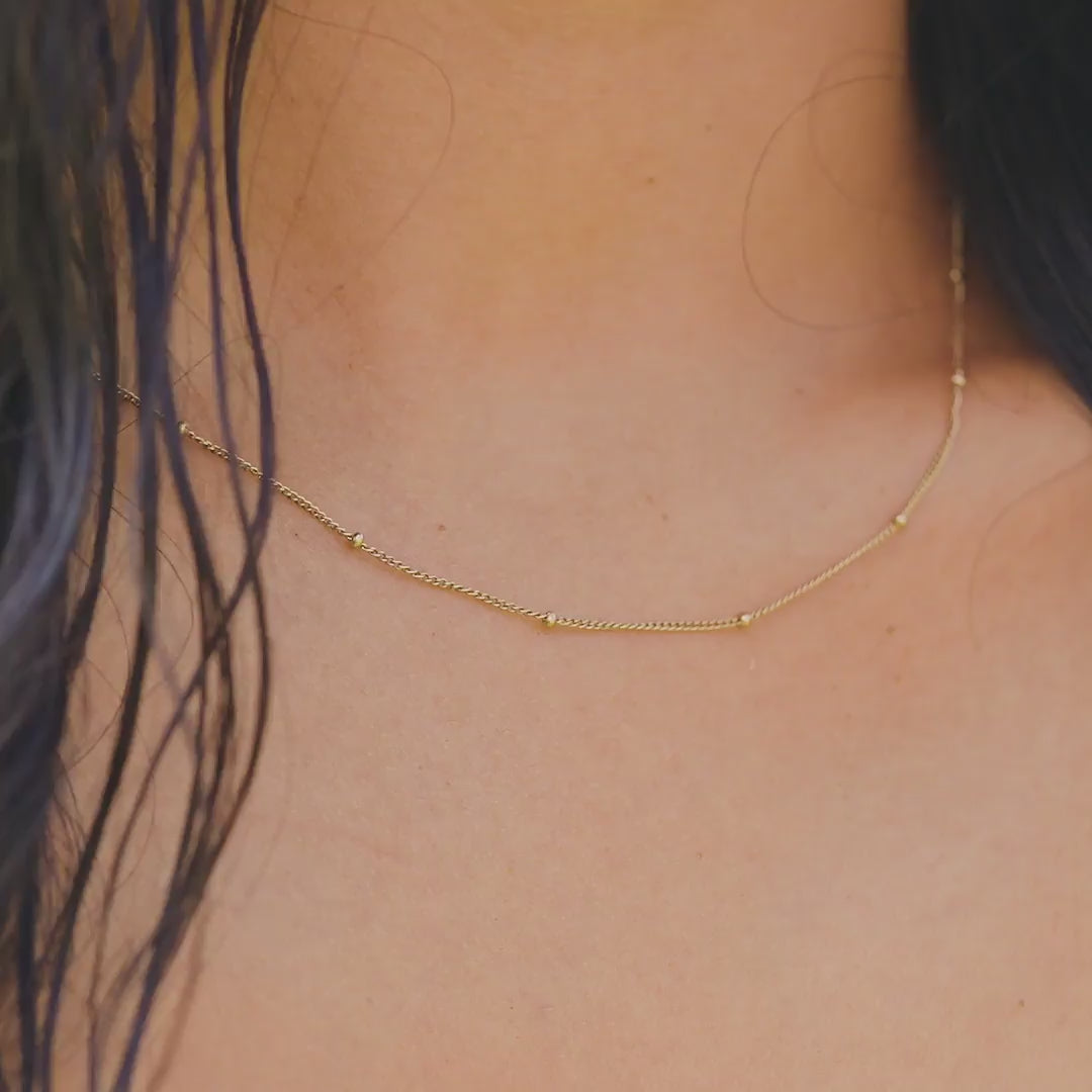 video of a dainty 14k gold pvd plated stainless steel satellite chain necklace on a model at the beach