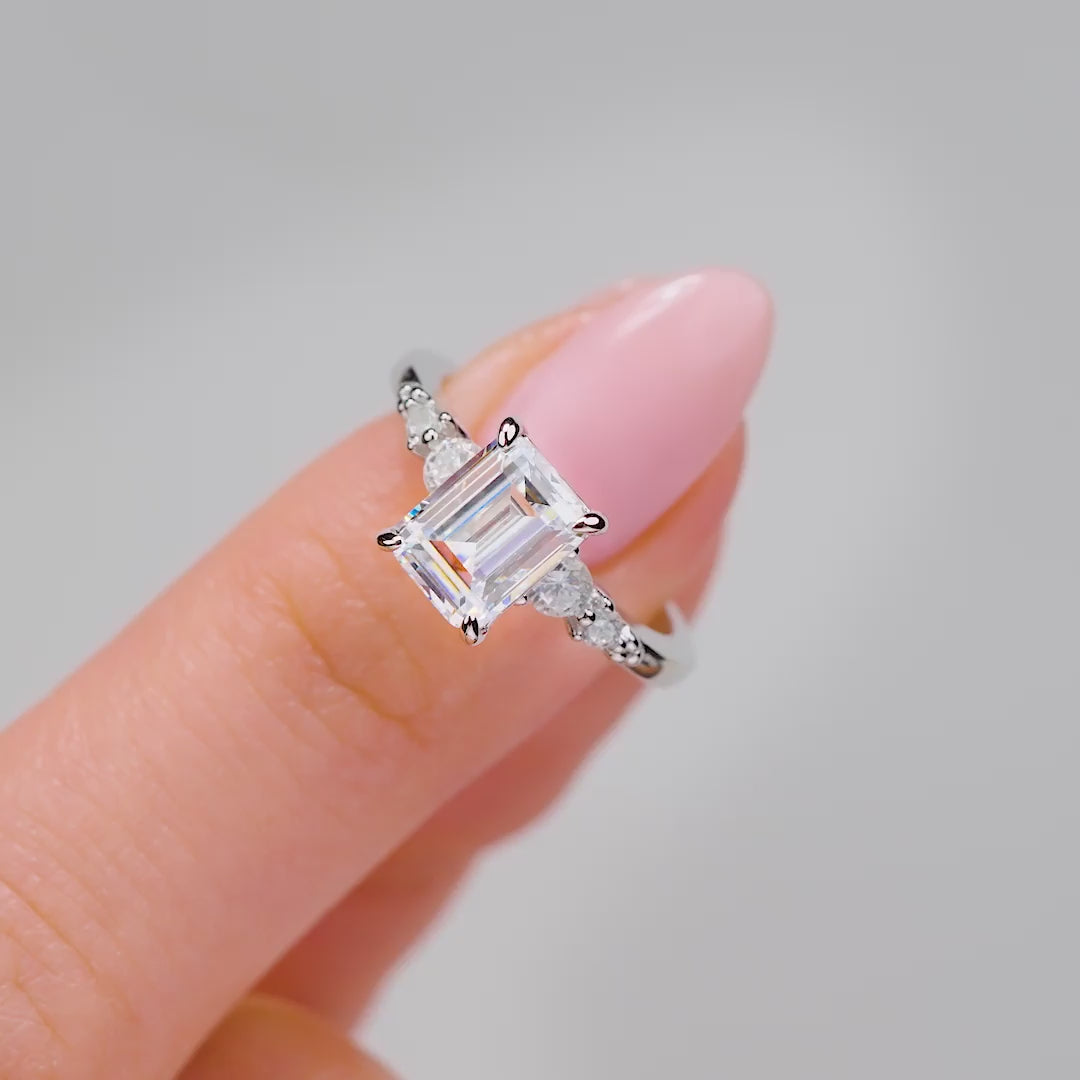 video of stunning silver 1.5 carat emerald cut engagement ring worn by model with light pink nails