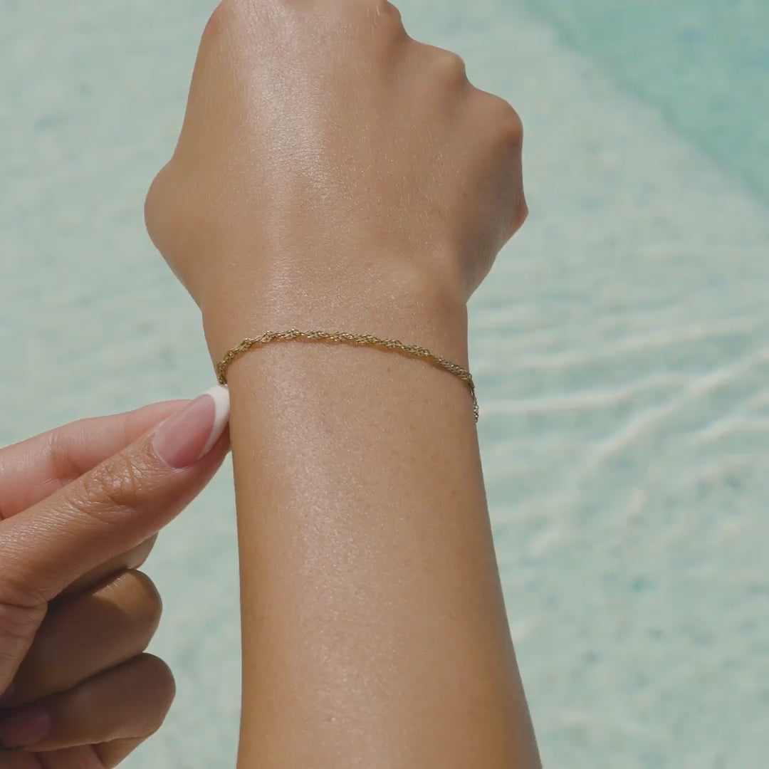 video of a 14k gold PVD plated stainless steel singapore chain bracelet with an extender on a model at the pool with french tip nails